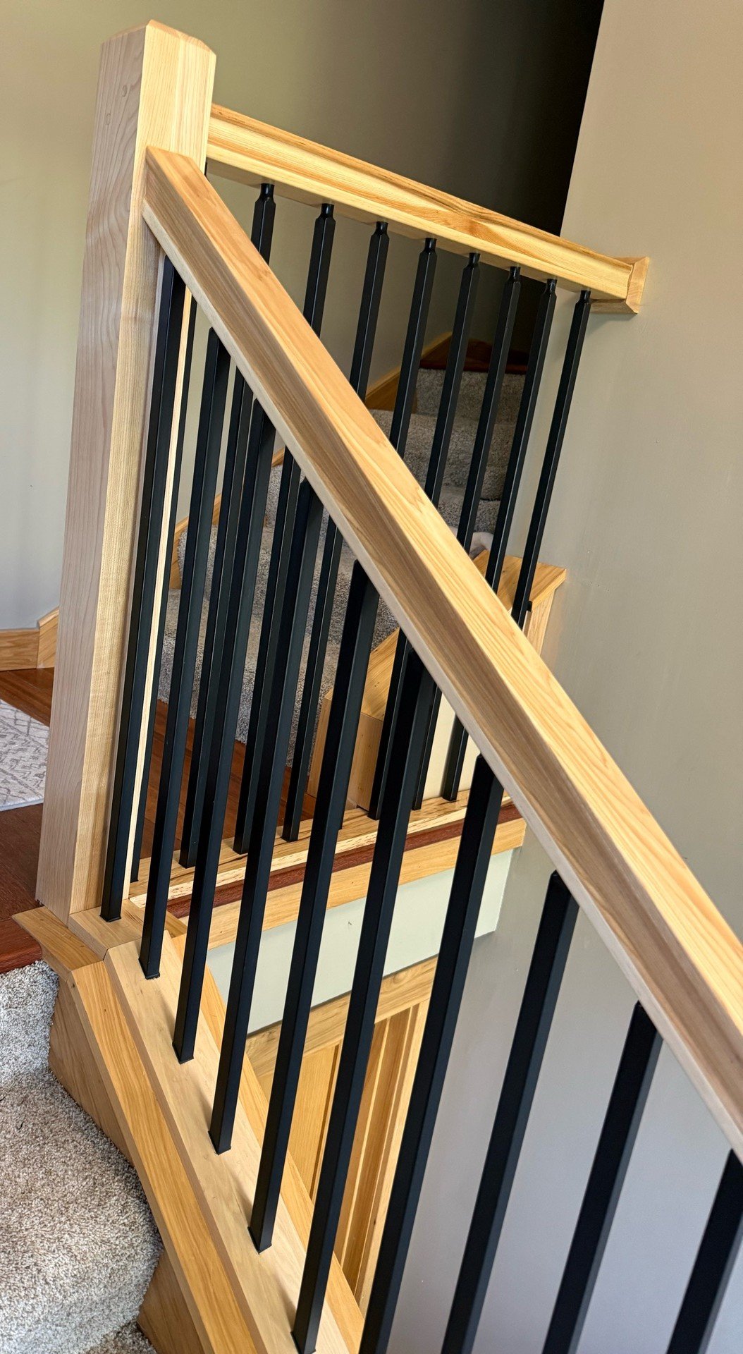 Close-up of custom hickory stair railing and black baluster installation in Fridley Minnesota