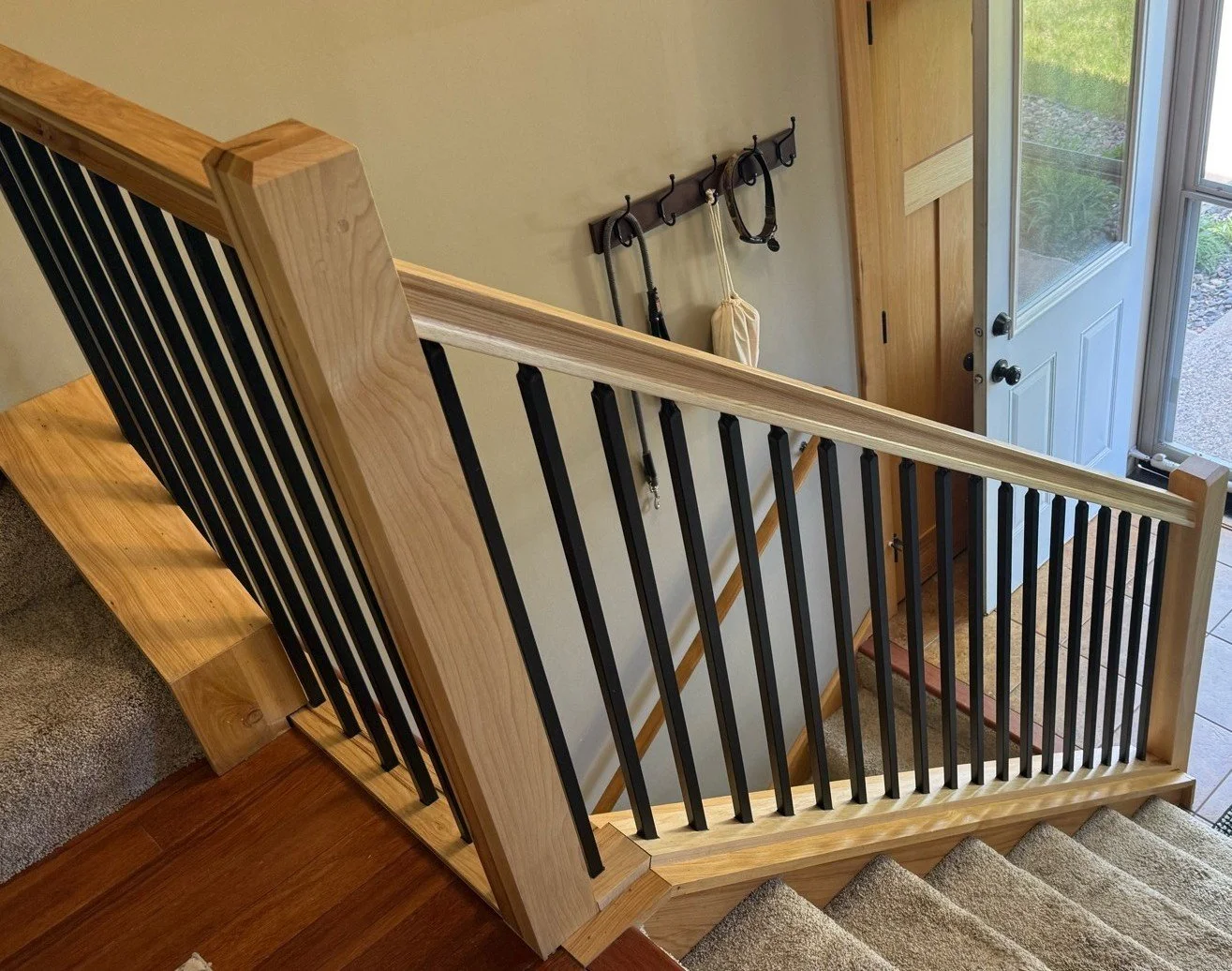Modern stair railing installation with black metal balusters and hickory handrail in Fridley MN