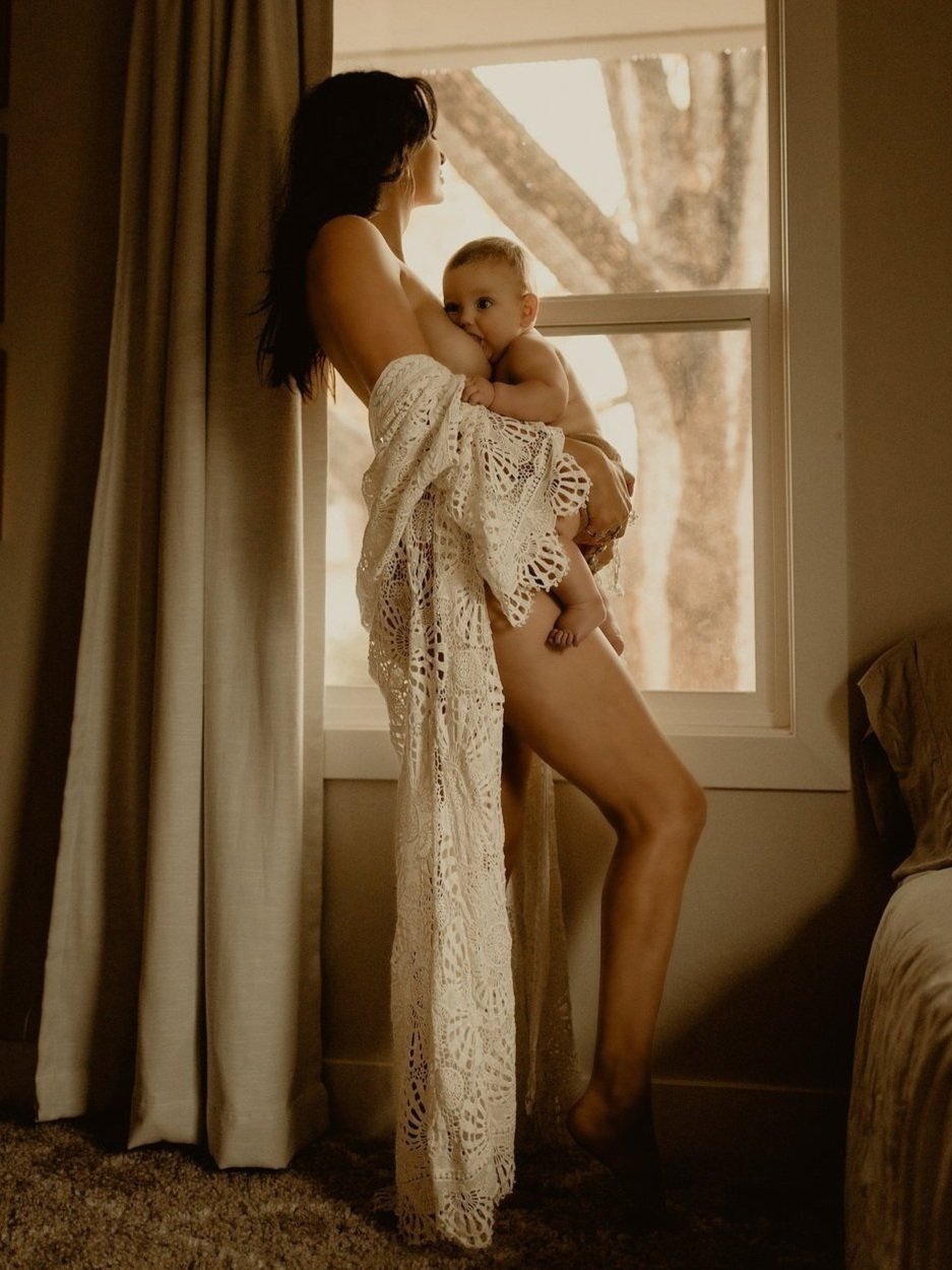 Mother+feeding+baby+by+window+drapped+in+white+newborn+family+portraits.jpg