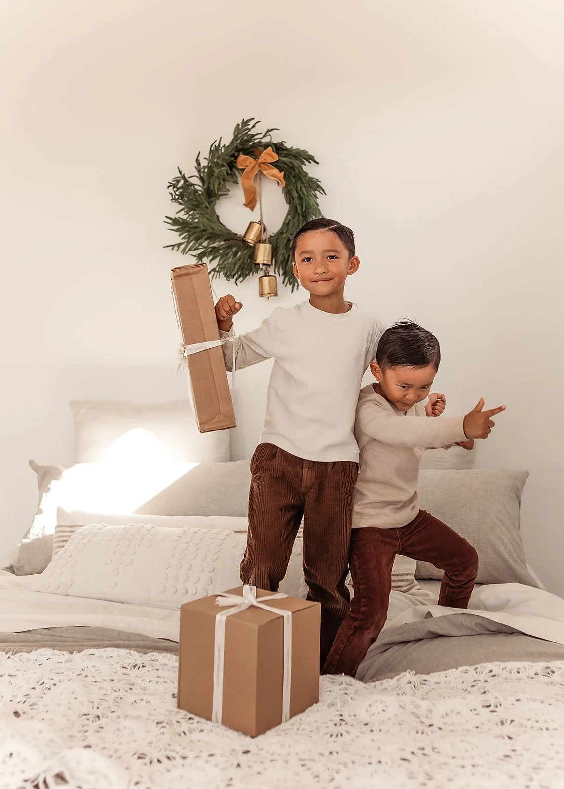 Two kids with presents on a bed, a holiday wreath hanging on the wall behind them, perfectly capturing the magic of childhood moments, as seen through the lens of a Roseville family photographer.