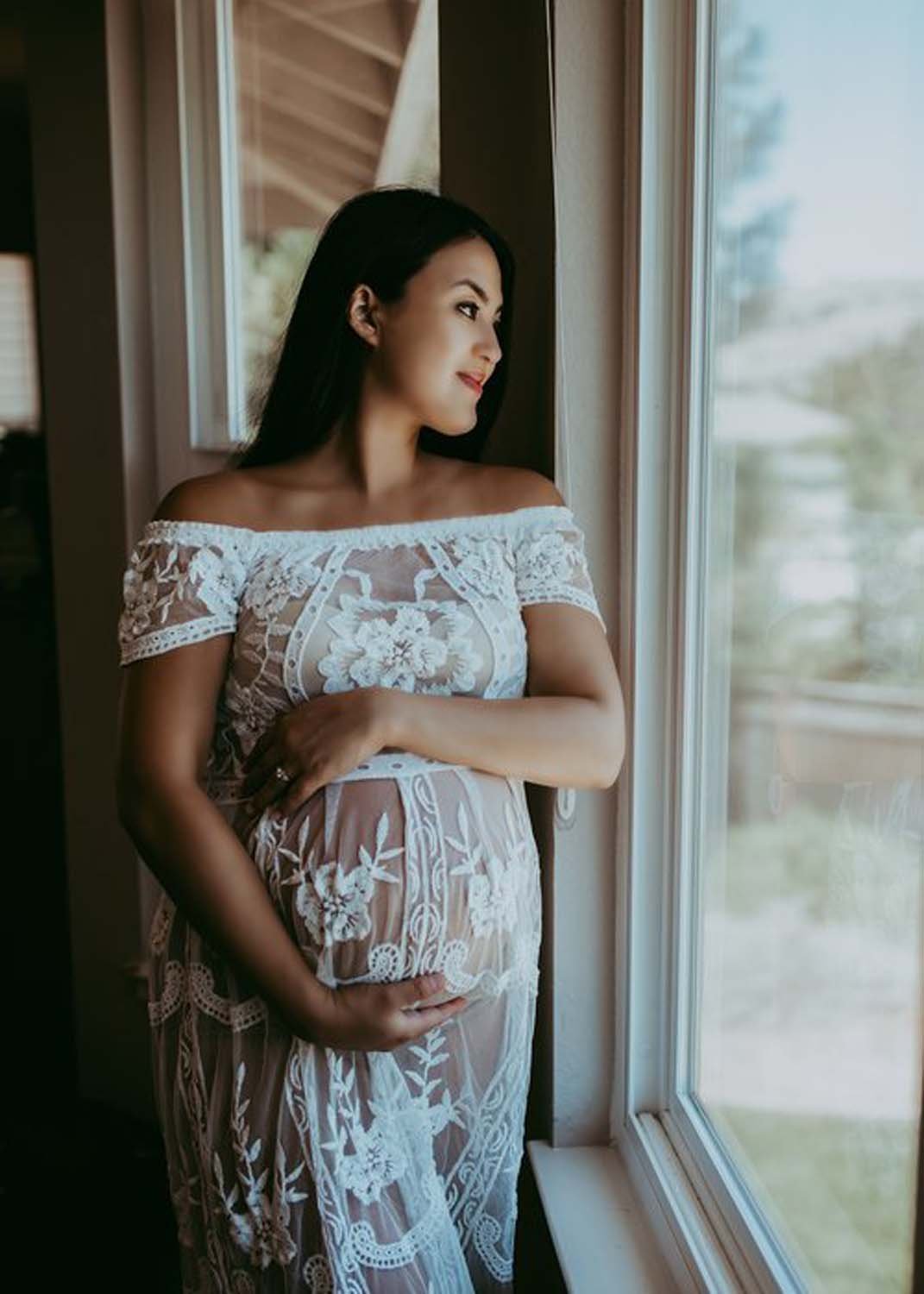 Pregnant woman by window holding belly maternity shoot photography Sacramento.jpg