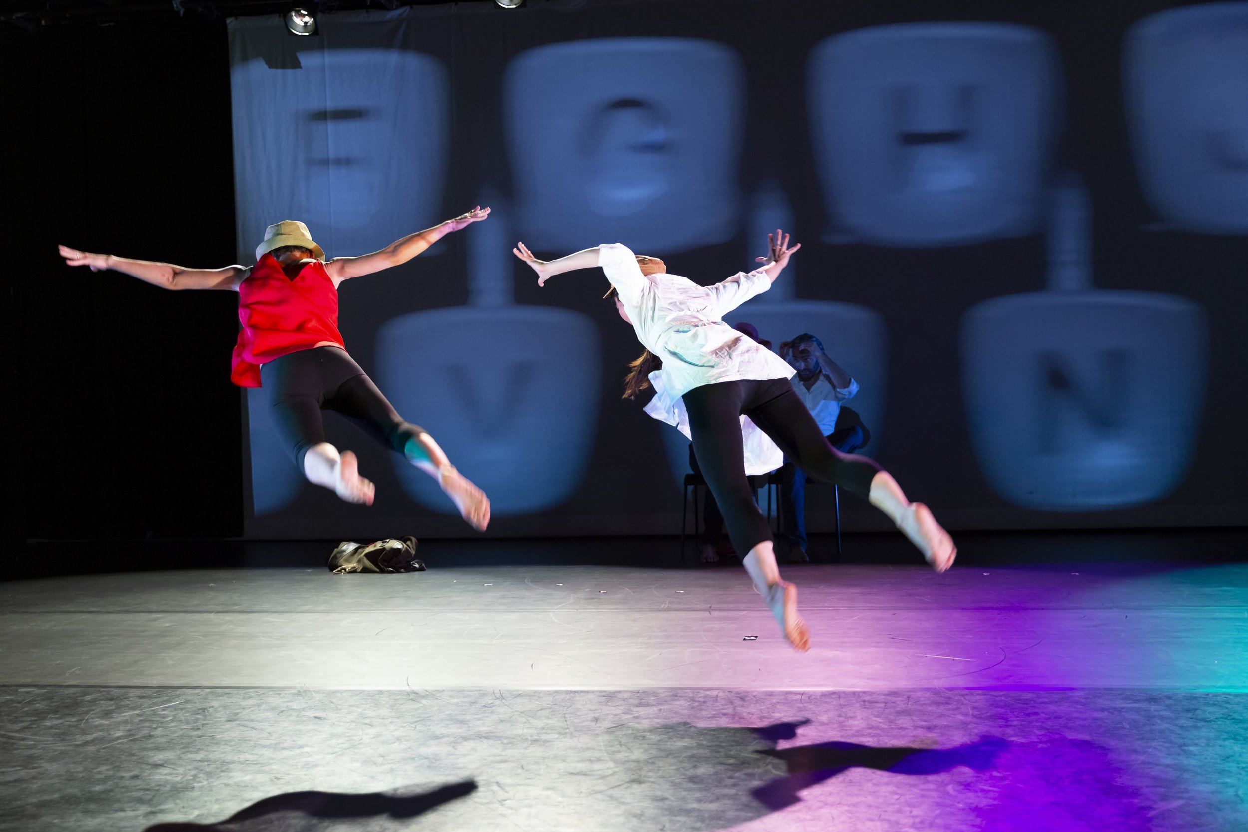 Valentina Priolo and Motoko Tadano gracefully suspended in the air on a stage, during IDEN-defy performance at the HERE Center in New York City.