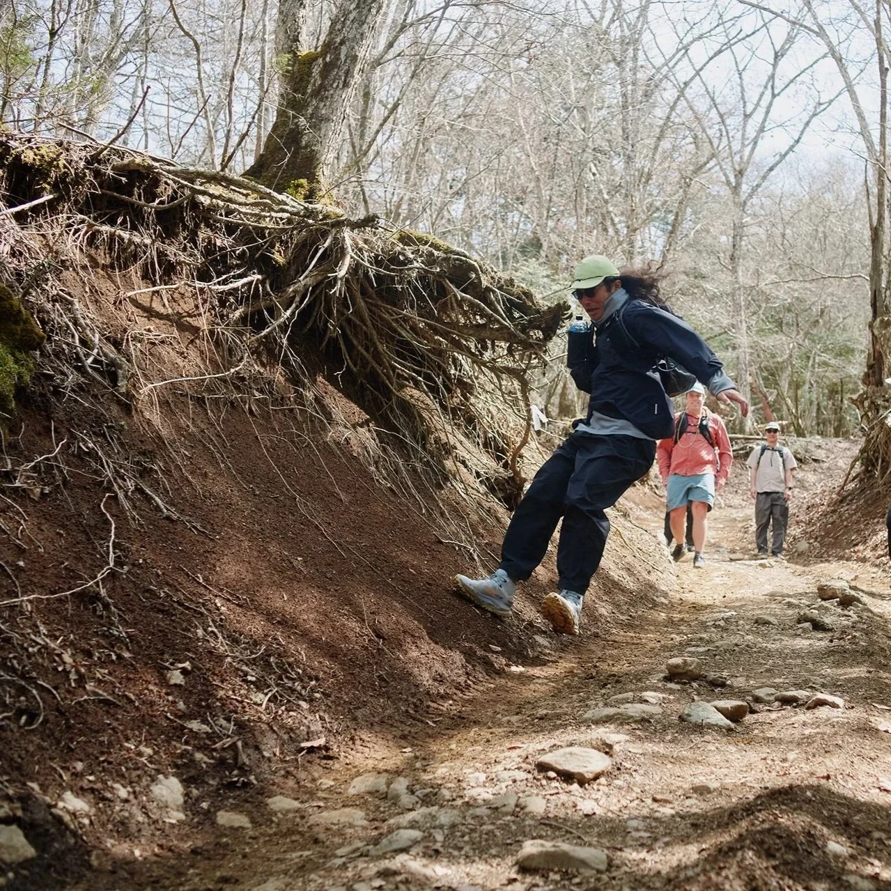 Man in jumping motion in the middle of the trail wearing light and cooling outdoor apparel and headwear accessory.