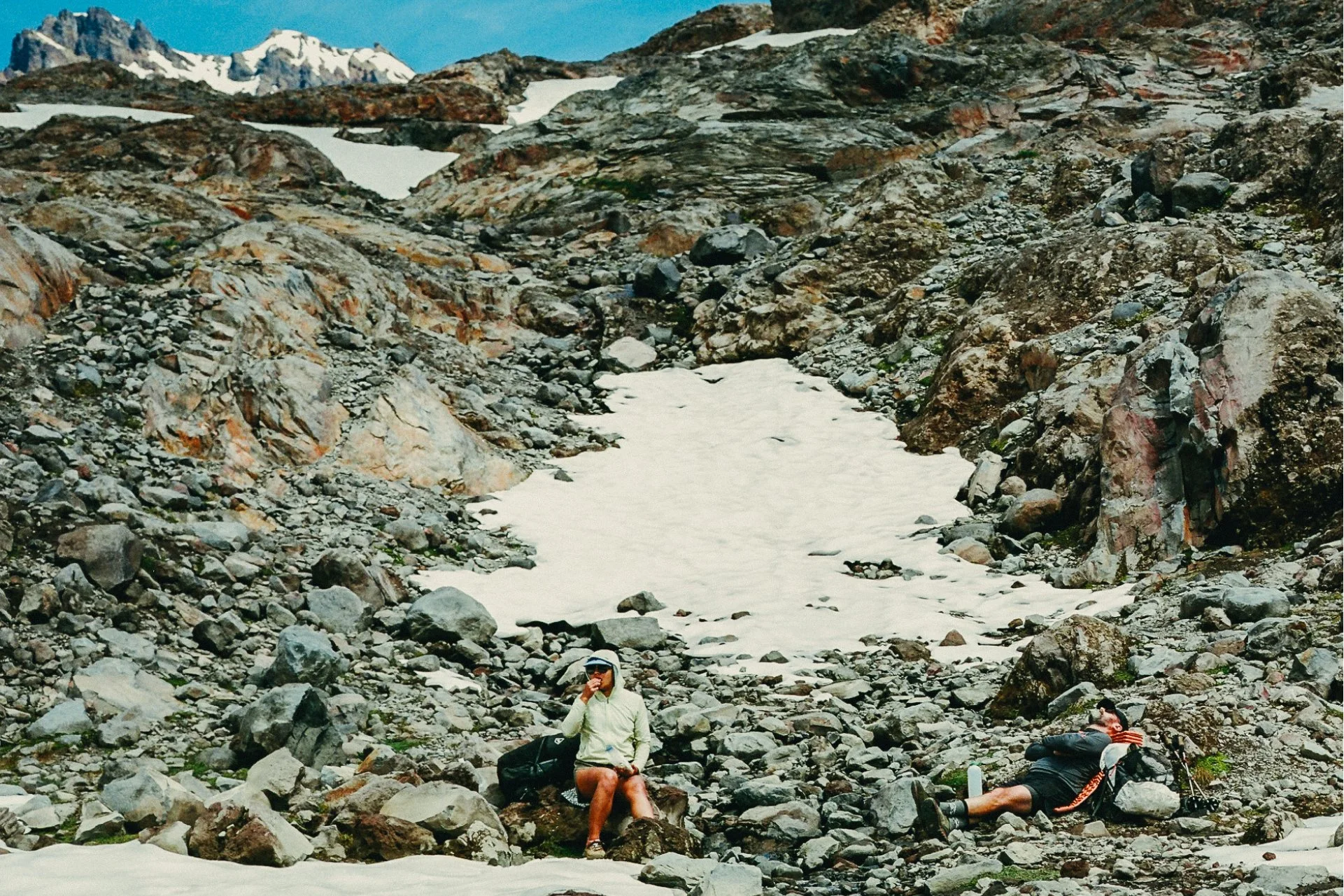 Two hikers wearing Parapack hats resting in a rocky section of trail. 5-panel sport cap, ultra lightweight, breathable mesh, compact, moisture wicking, unisex, UPF 50 headwear for travel, hiking, urban outdoors, photo by Jamie Cooper