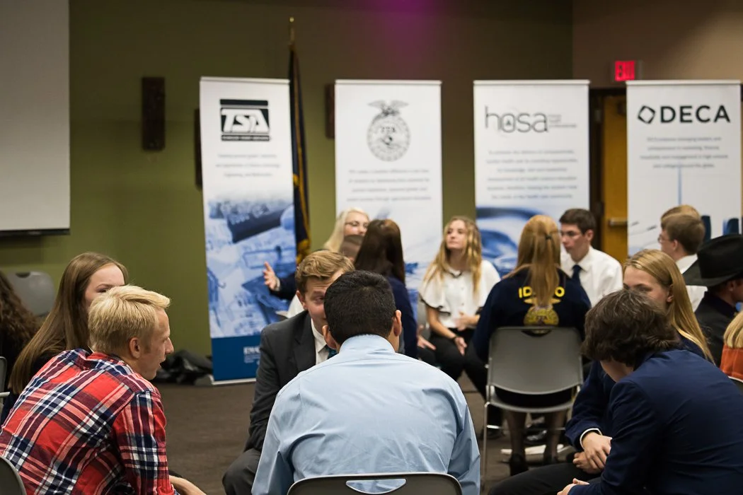 Group of young people participating in a panel discussion or group activity in a conference room, with informational banners in the background.