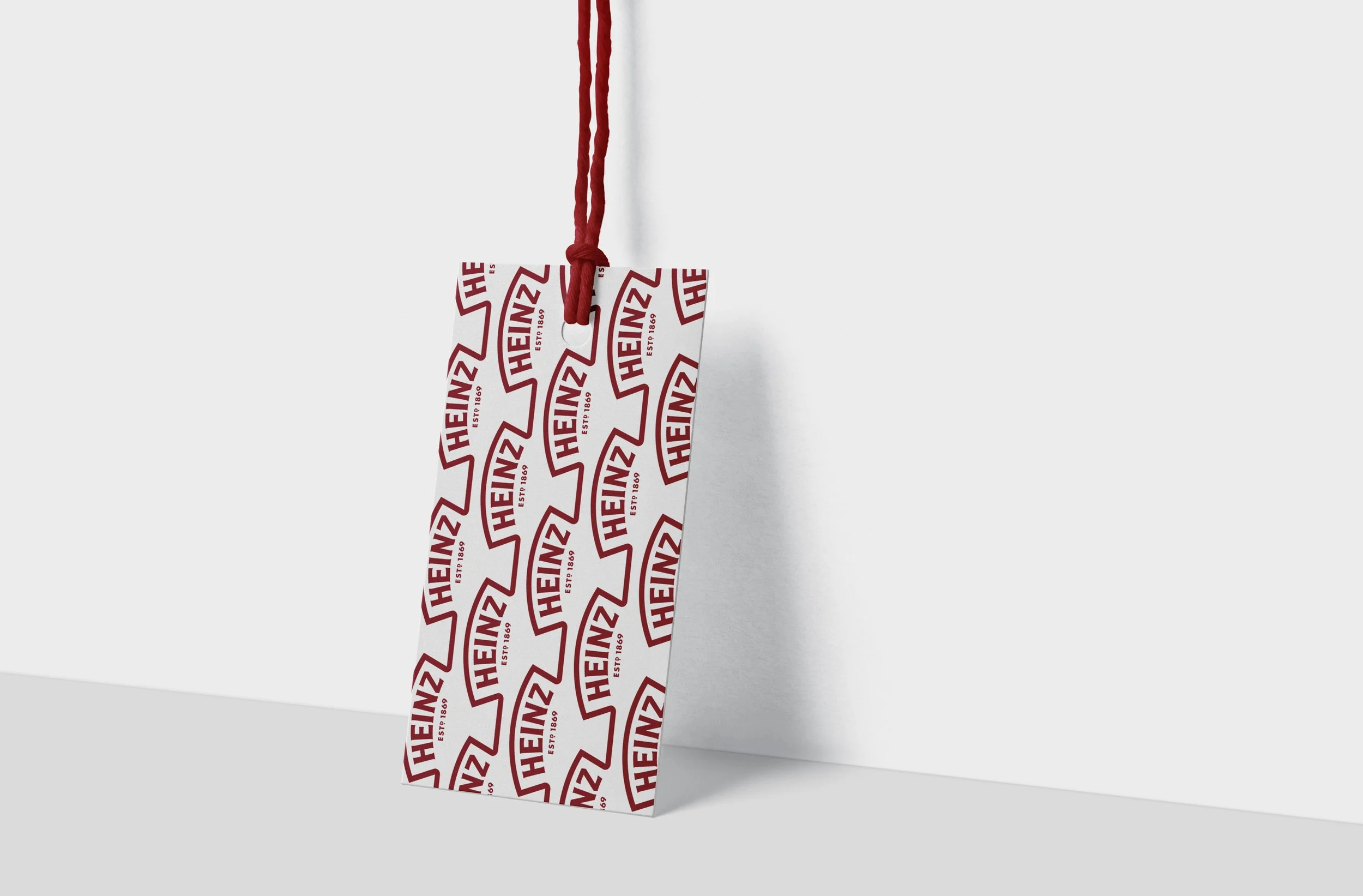 Gift bag with Heinz logo pattern and red handles against white background.