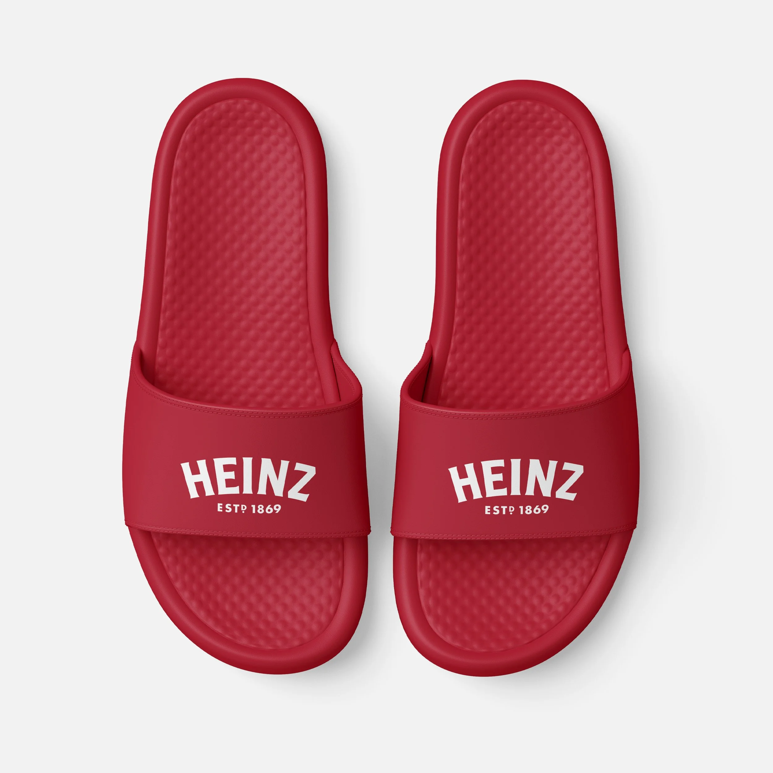 Red slide sandals with white Heinz logo and 'Est. 1869' printed on the straps, placed against a white background.