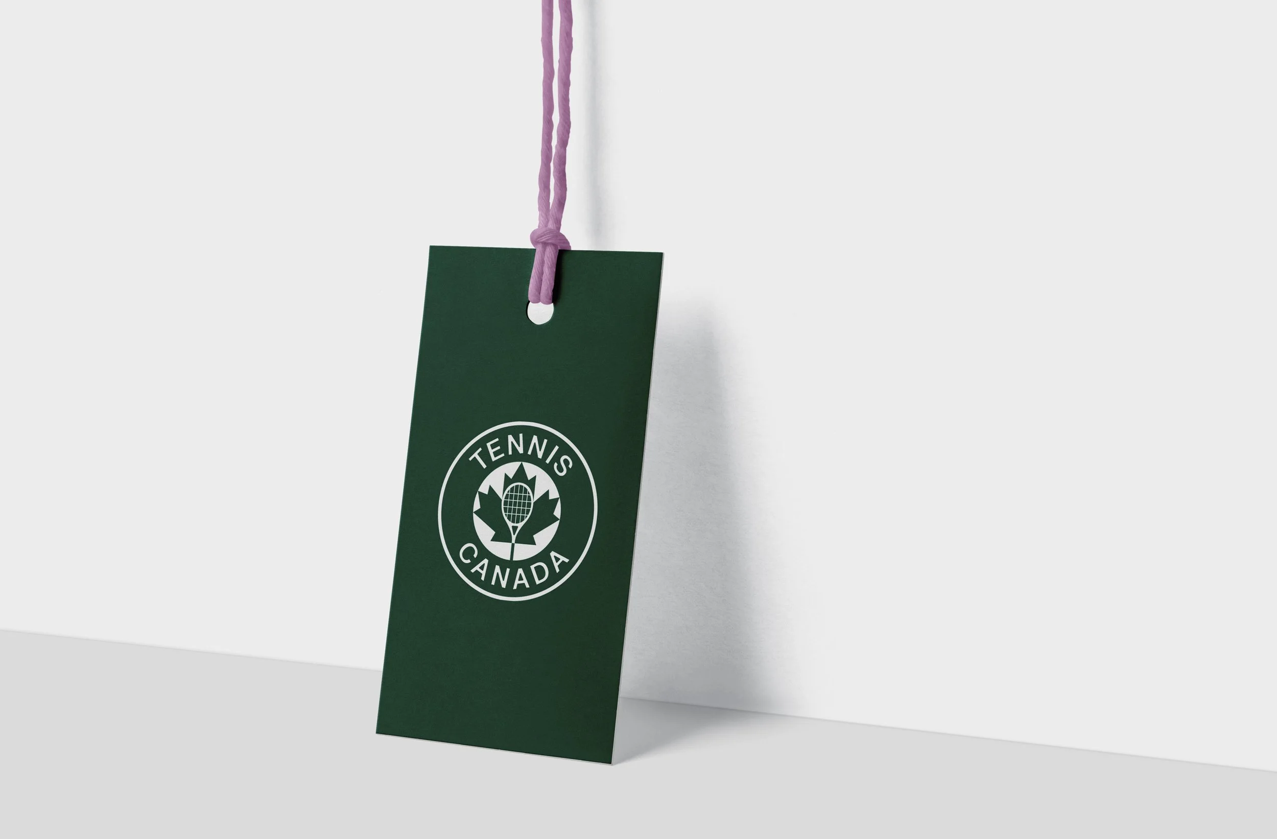 A green tag with the Canadian Tennis Association logo hanging from a purple string tied to a white wall.
