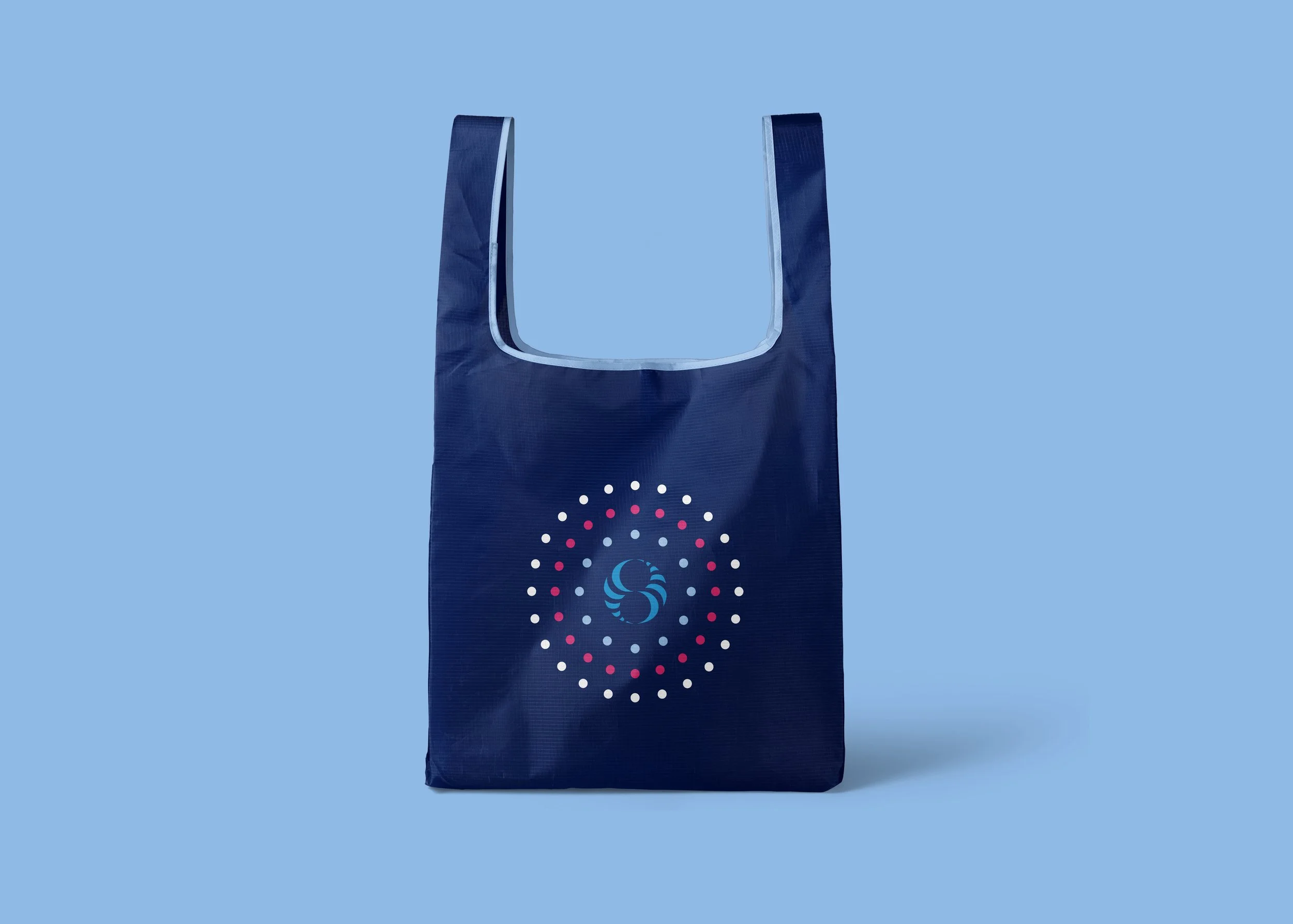 A dark blue reusable shopping bag with a colorful, circular logo in the center, standing against a light blue background.