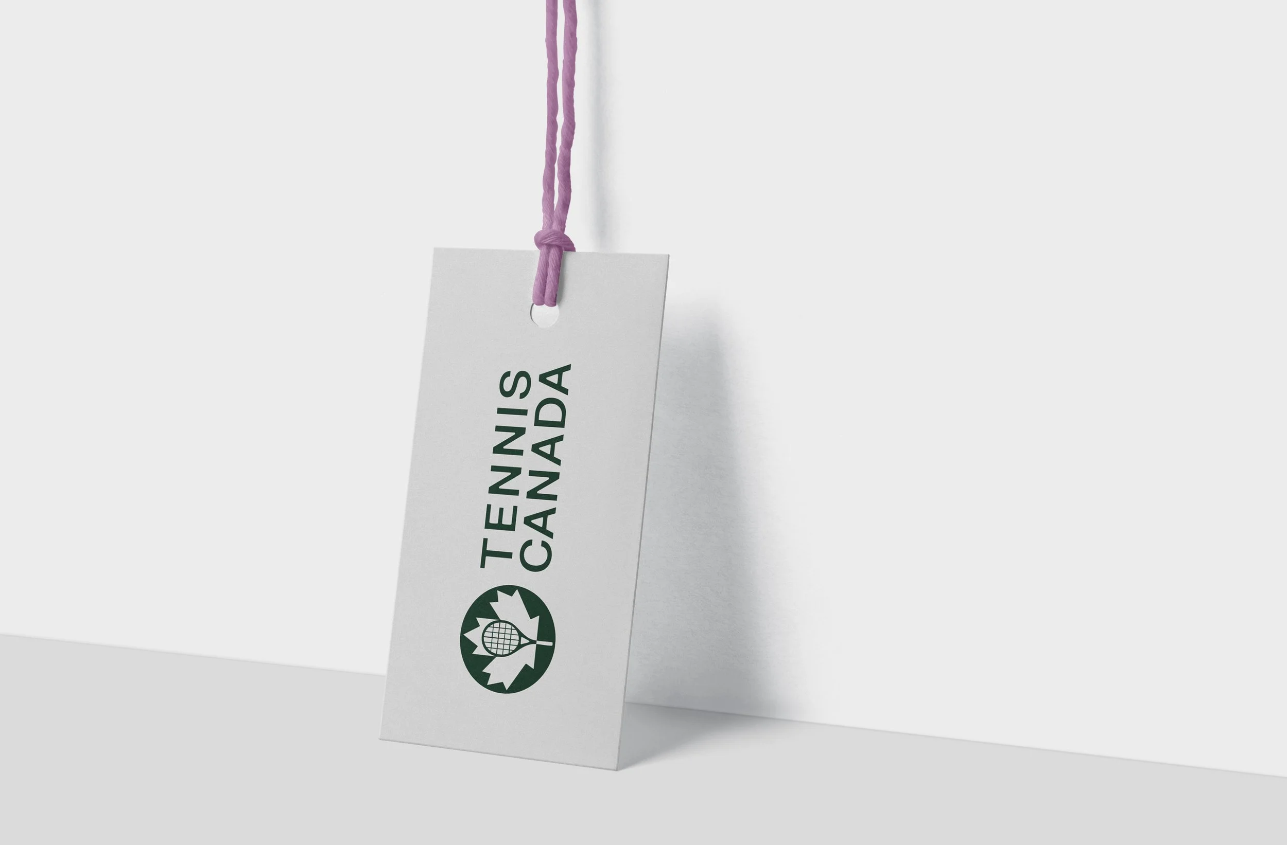 A white tag hanging from a pink string with a knot at the top. The tag has black text that reads "TETE NIS CAUDA" and a barcode below.