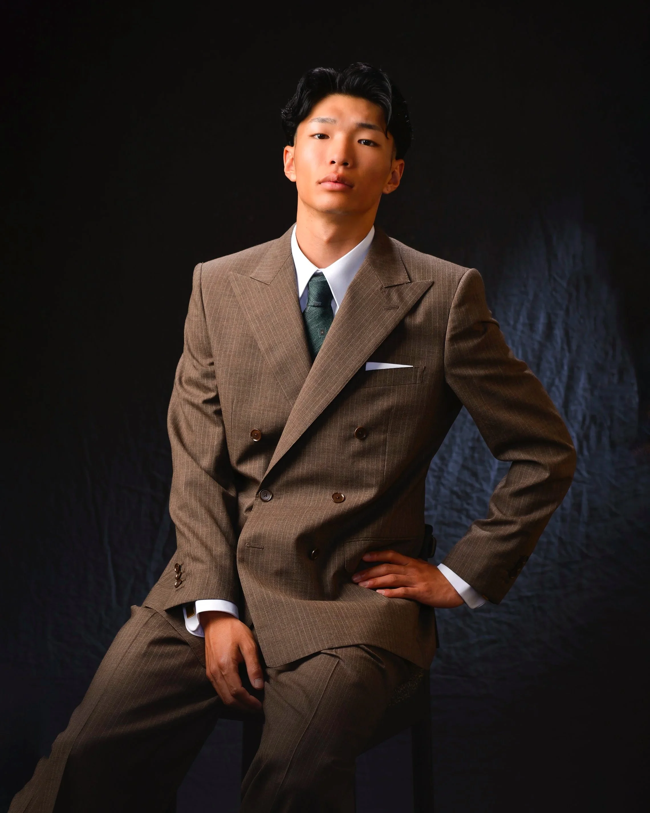 茶色のスーツを着た若い男性がポーズをとっている