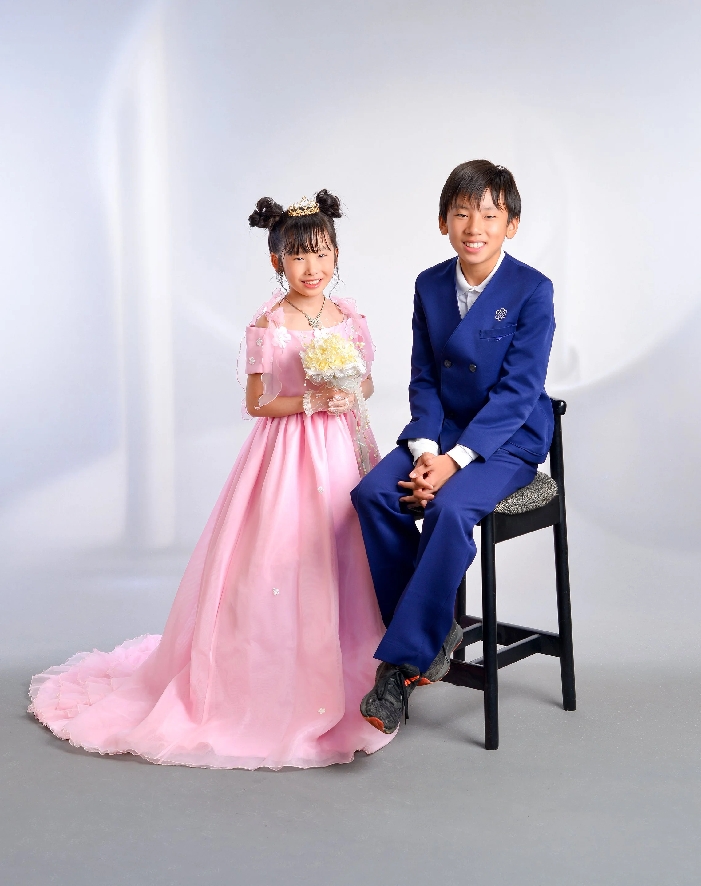 ピンクのドレスを着た少女と青いスーツを着た少年がスタジオでポーズをとっている写真