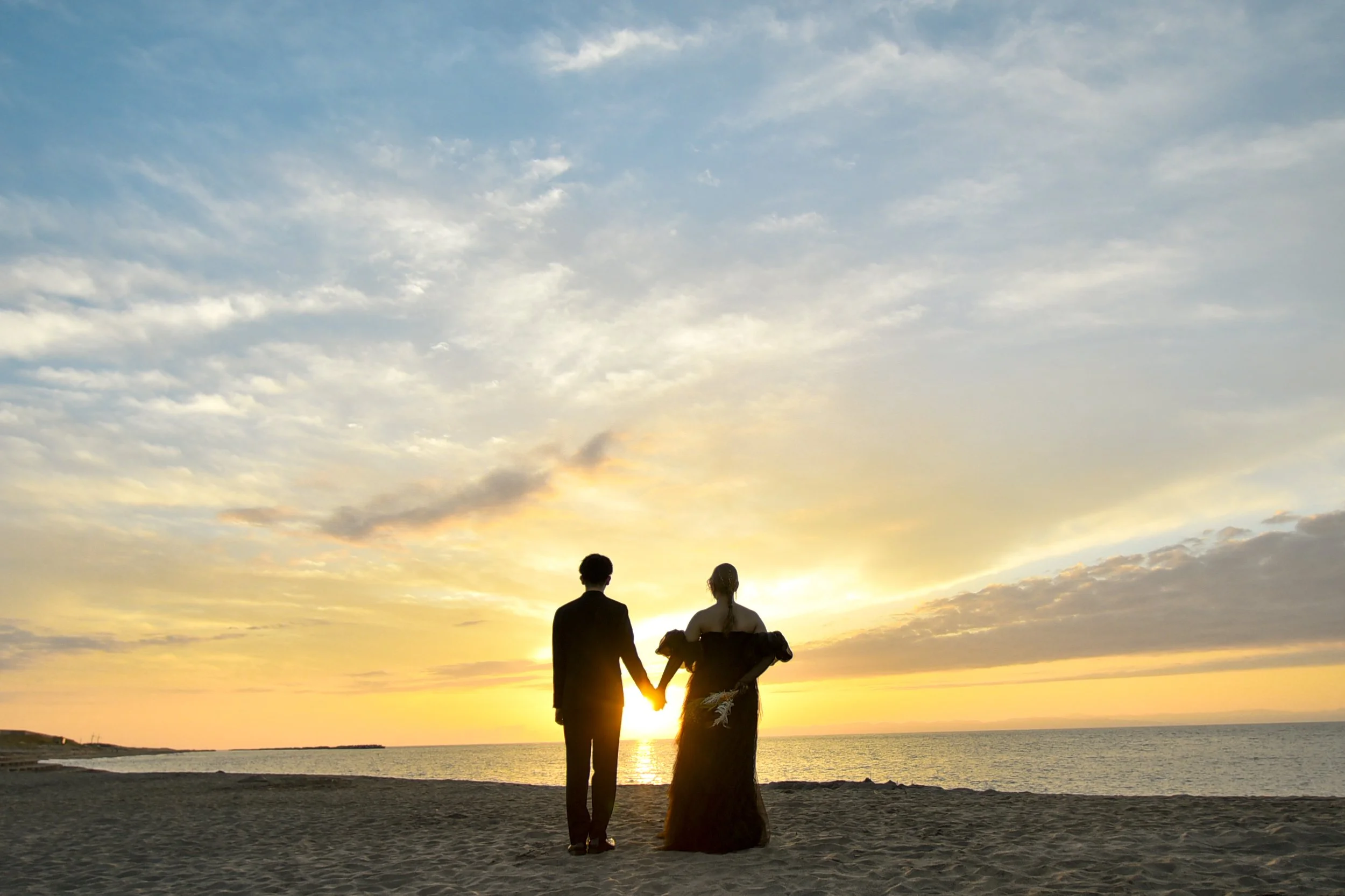 夕焼けの海辺で手をつなぐ男女のシルエット