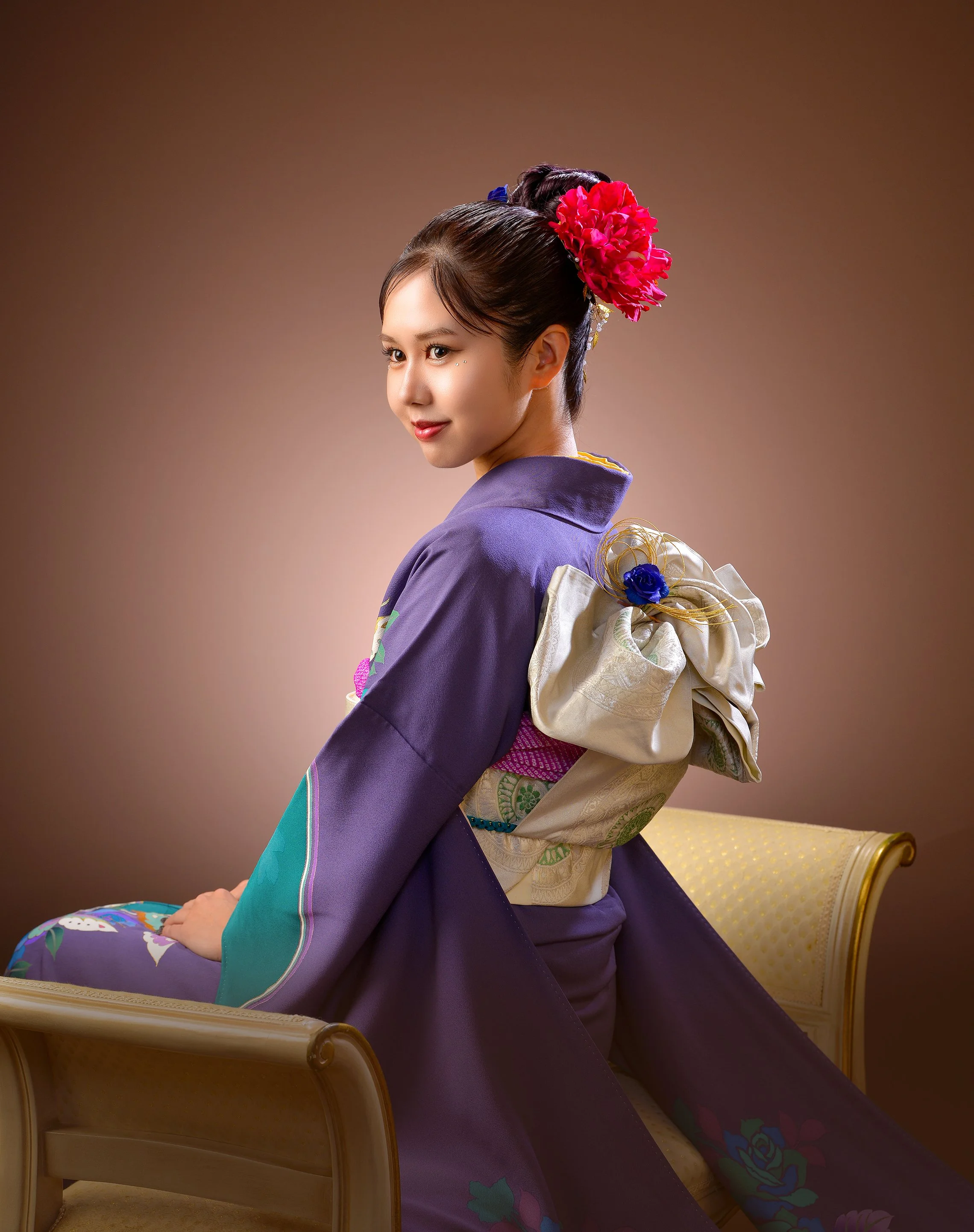 和服を着た若い女性が椅子に座っている。髪に大きな赤い髪飾りをつけている。
