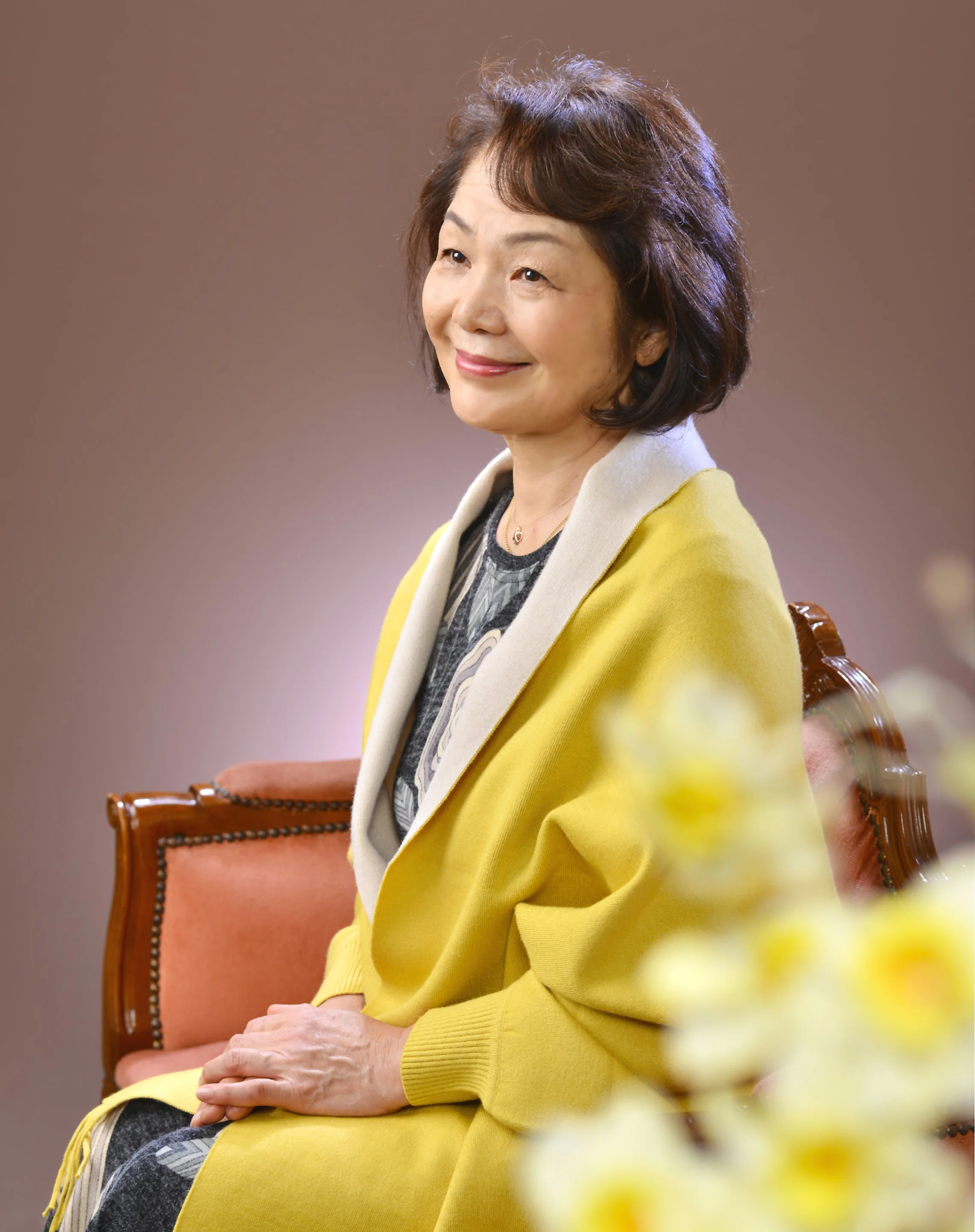 笑顔の中年女性が黄色いコートを着て座っている