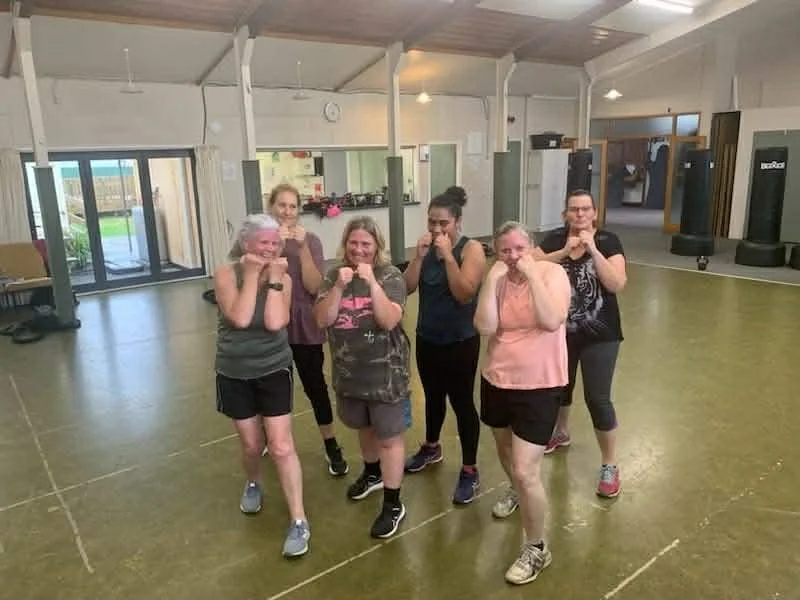 Six women in athletic clothing practice boxing in a church and punching bags.