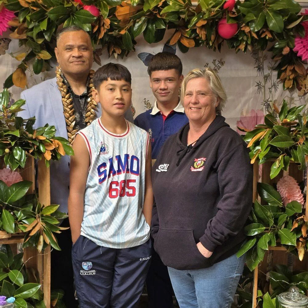 Four people standing among lush green leaves and pink flowers, smiling at the camera.