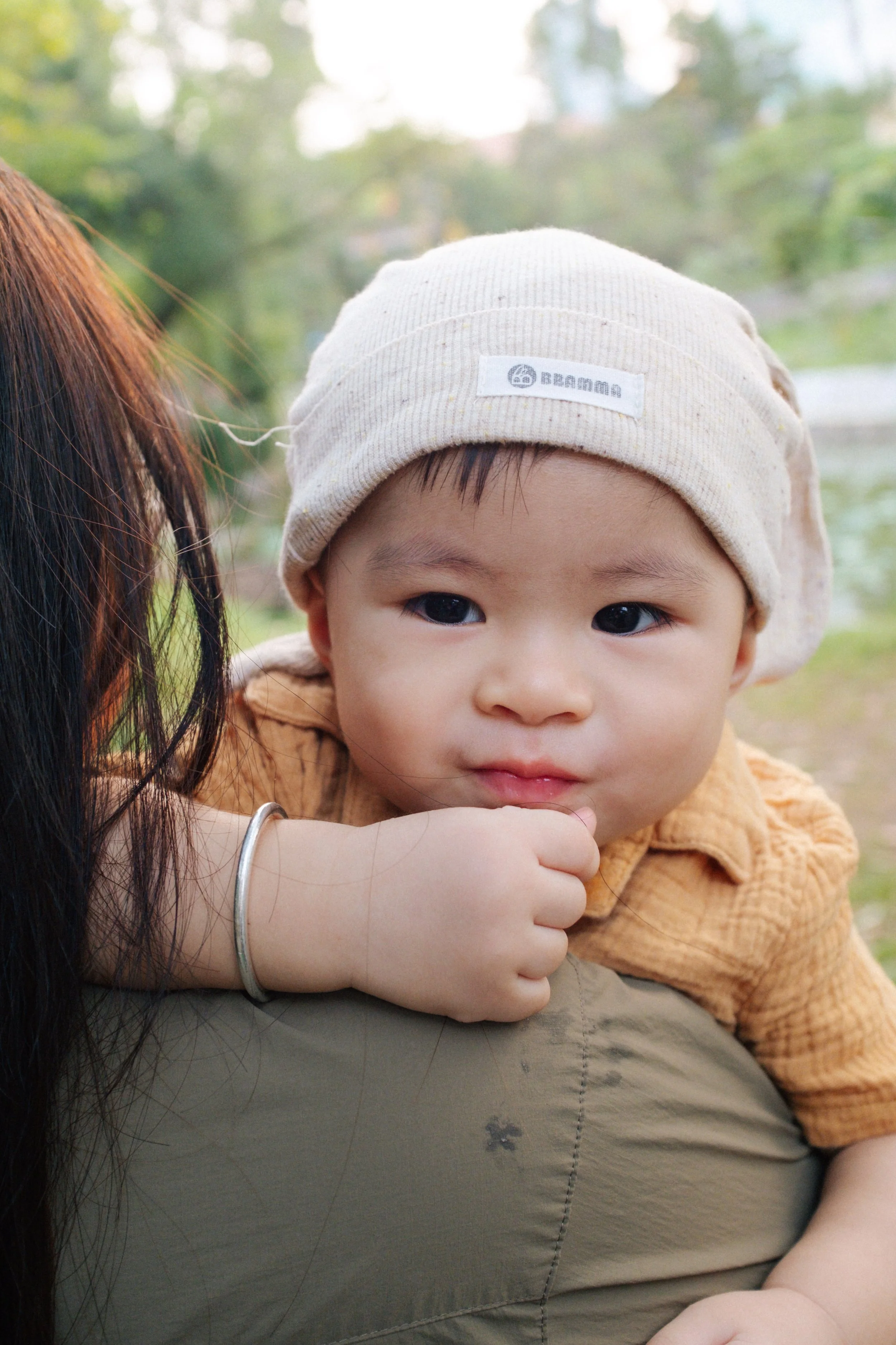 A young child with a beige hat resting on someone's shoulder outdoors.