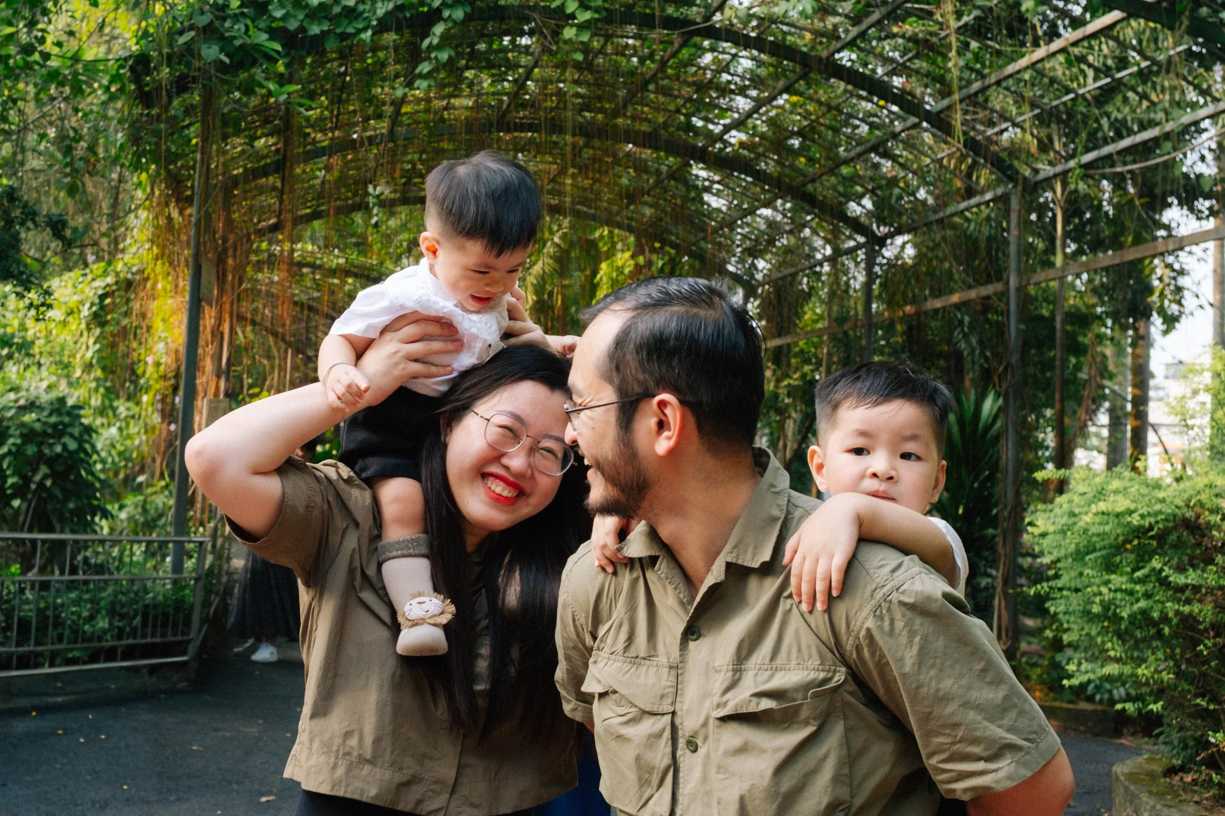 A smiling family of four, including two children, outdoors in a lush green garden or park, sharing a moment of joy and closeness.