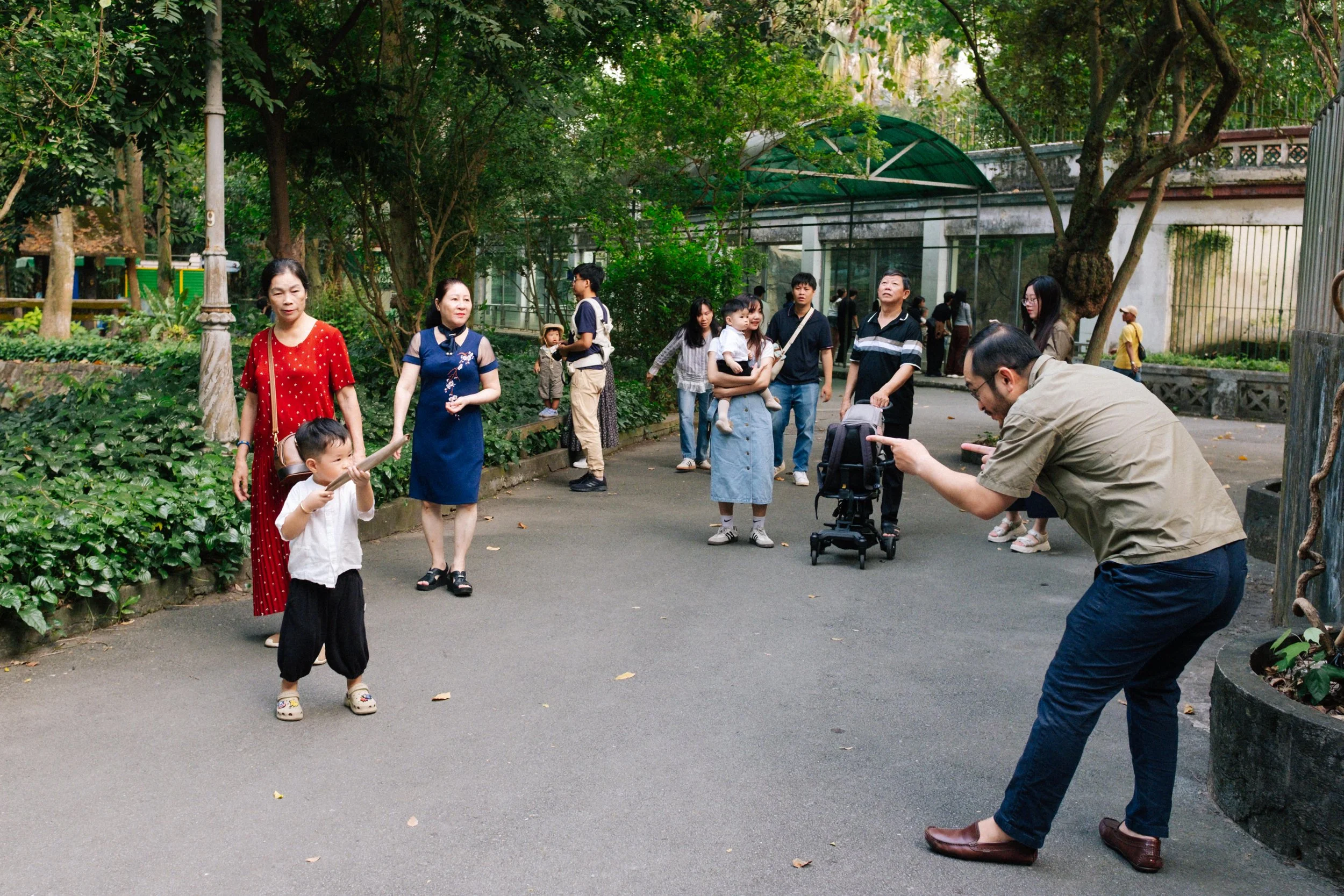 People in a park taking photos and walking, surrounded by trees and greenery.