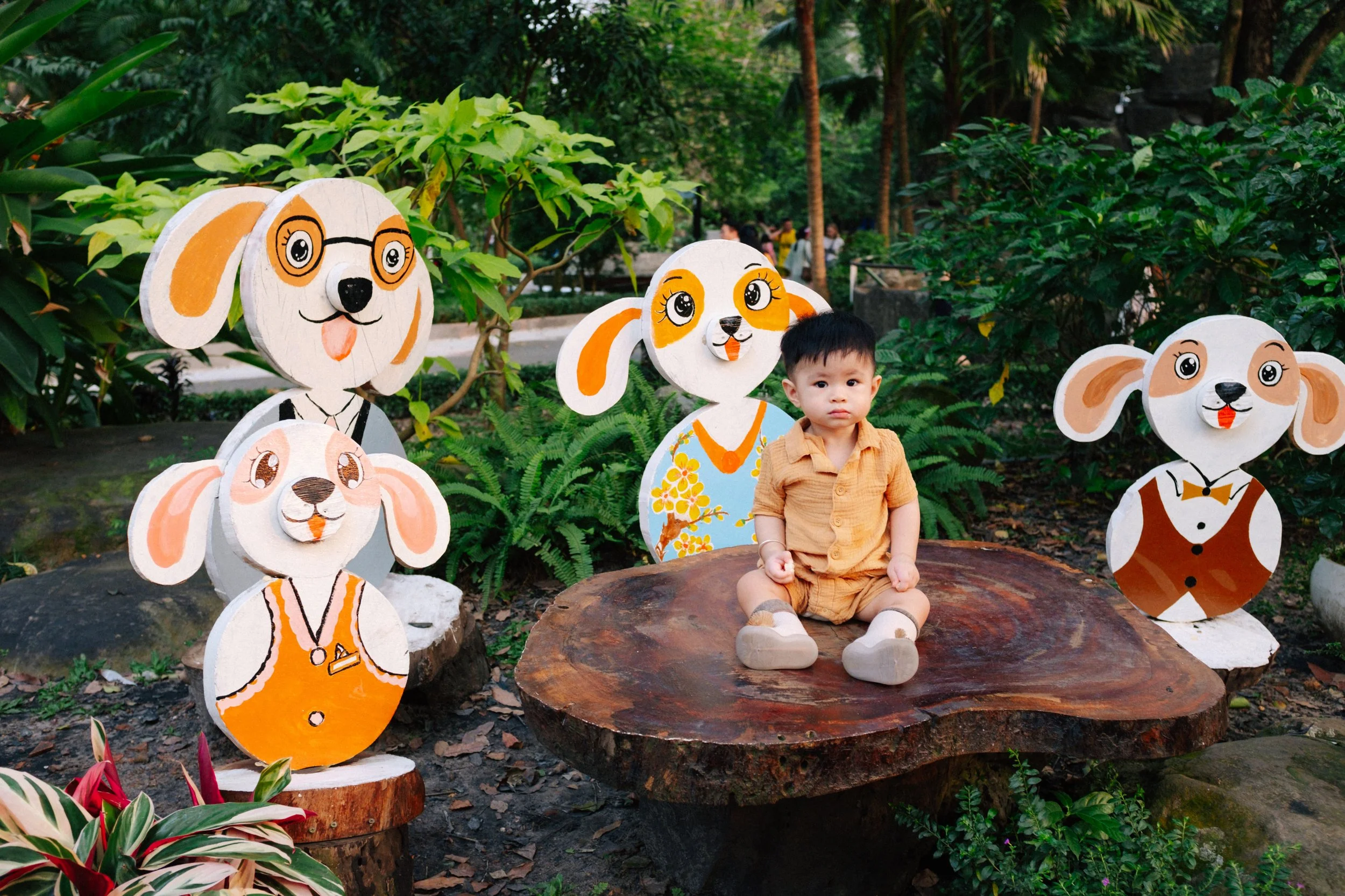 A young boy sitting on a large wooden platform surrounded by cartoonish dog-themed decorations in a garden.