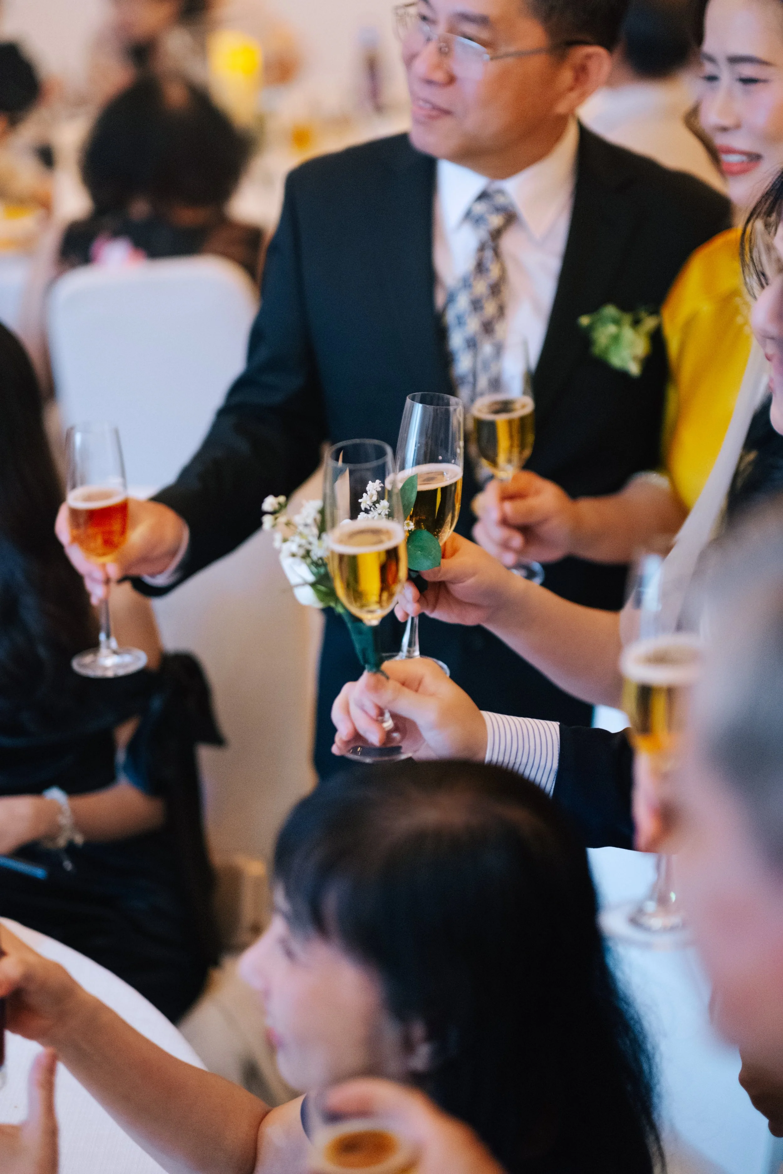 People raising champagne glasses in celebration at a formal gathering or wedding reception.