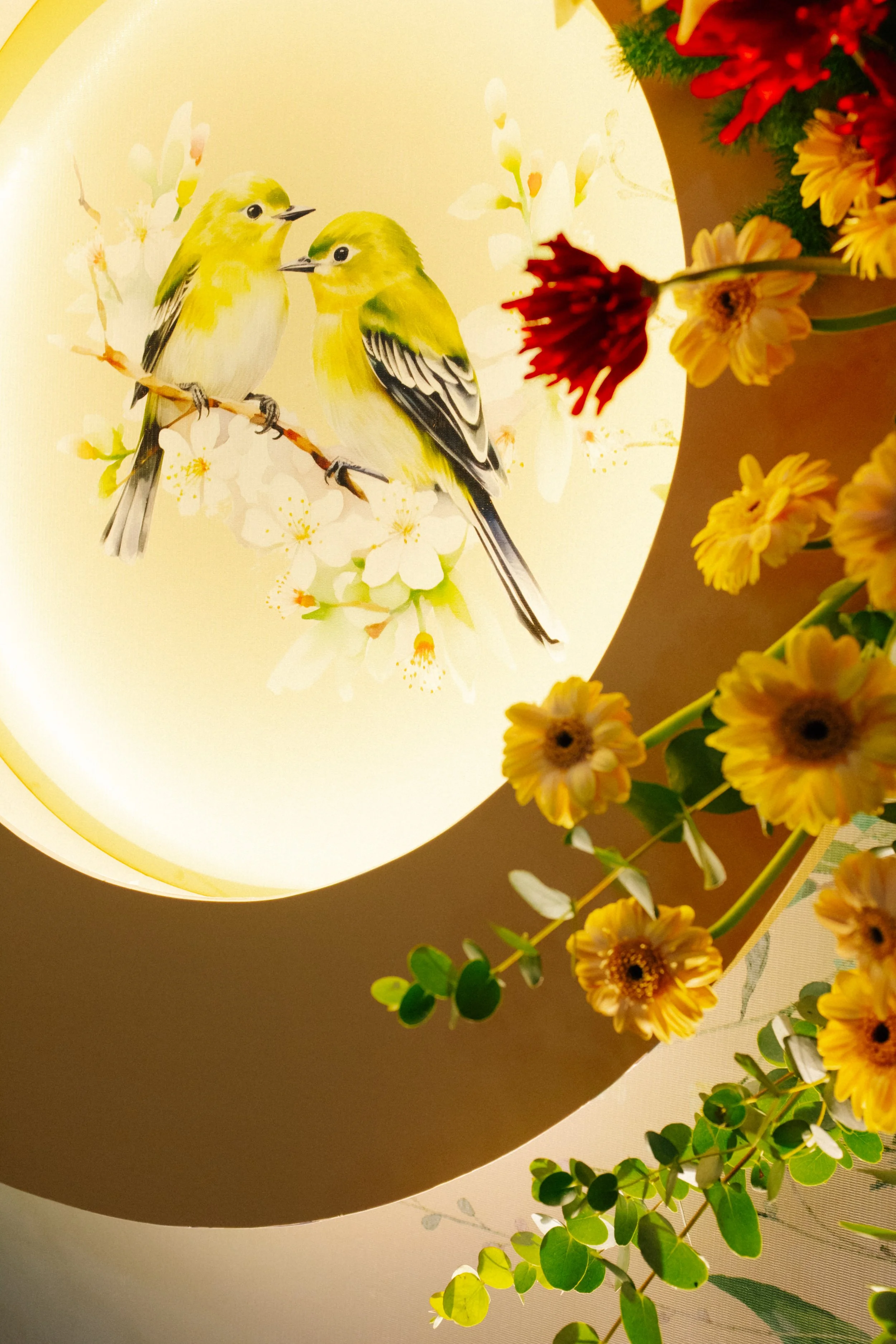 Decorative lamp featuring a painting of two yellow and black birds perched on a branch with white flowers, surrounded by yellow and red flowers and green foliage.