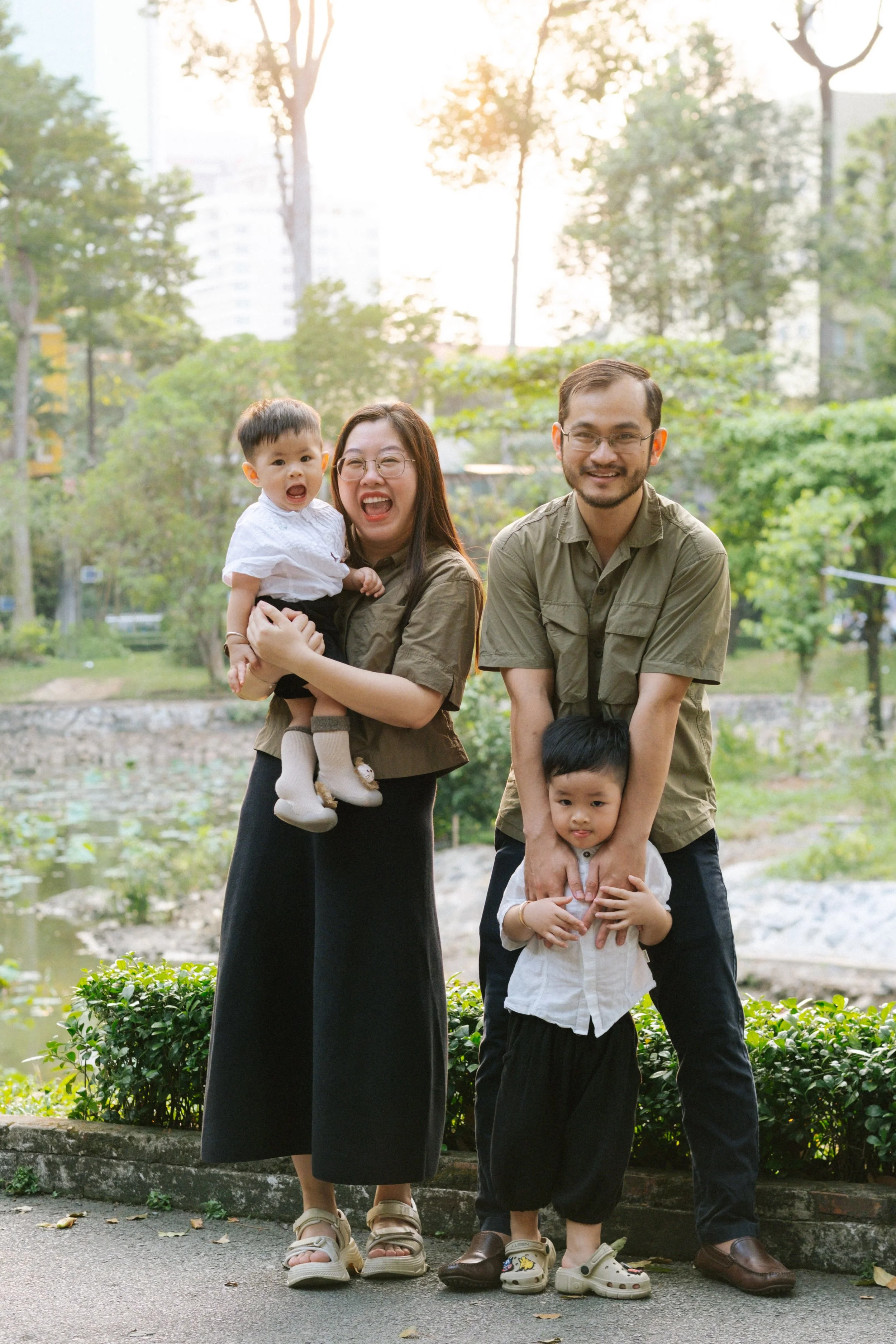 Happy family of four outdoors in a park, with two adults and two young children, smiling and posing for the photo.