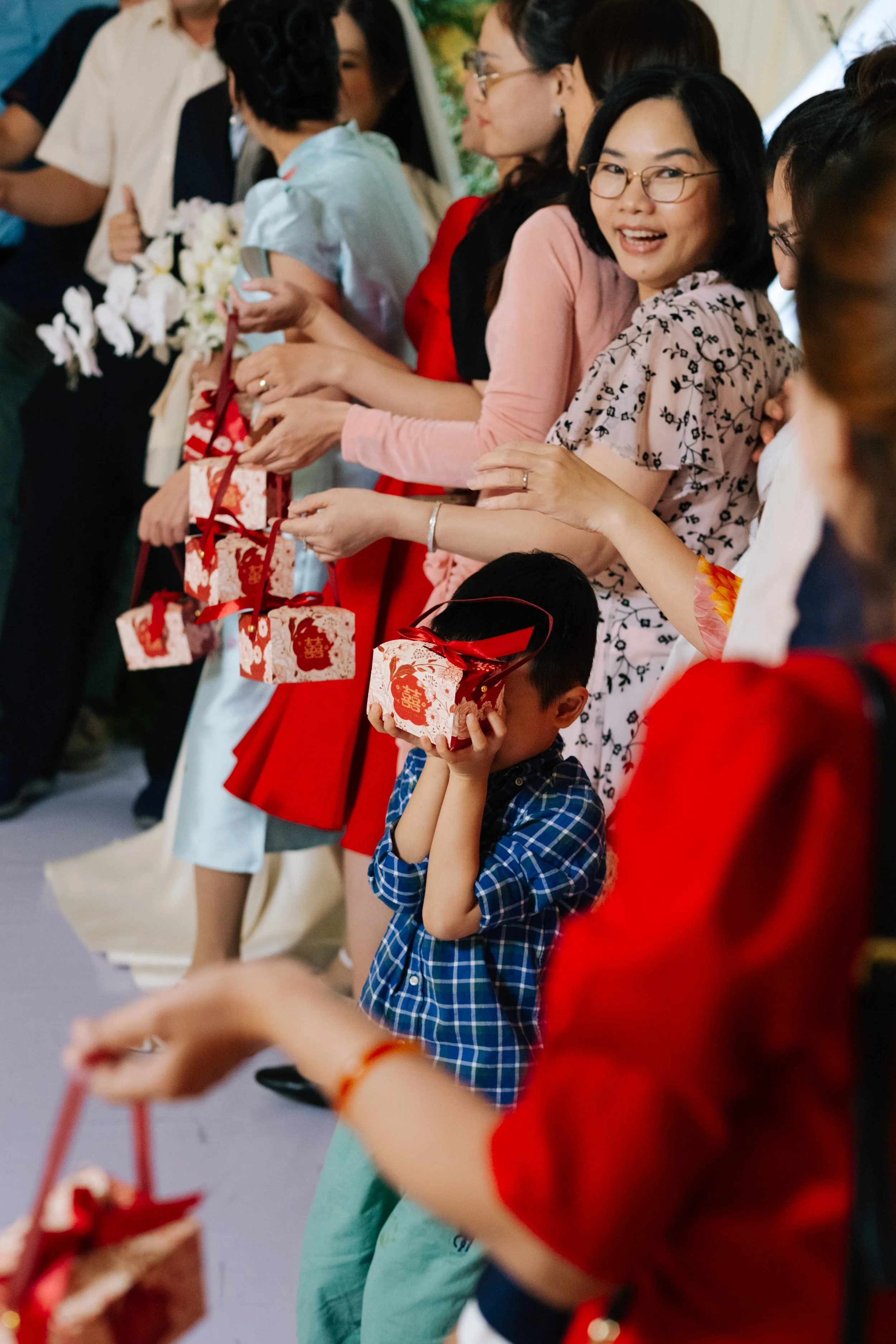 People participating in a gift exchange, holding decorated gift boxes with red ribbons, during a celebration.