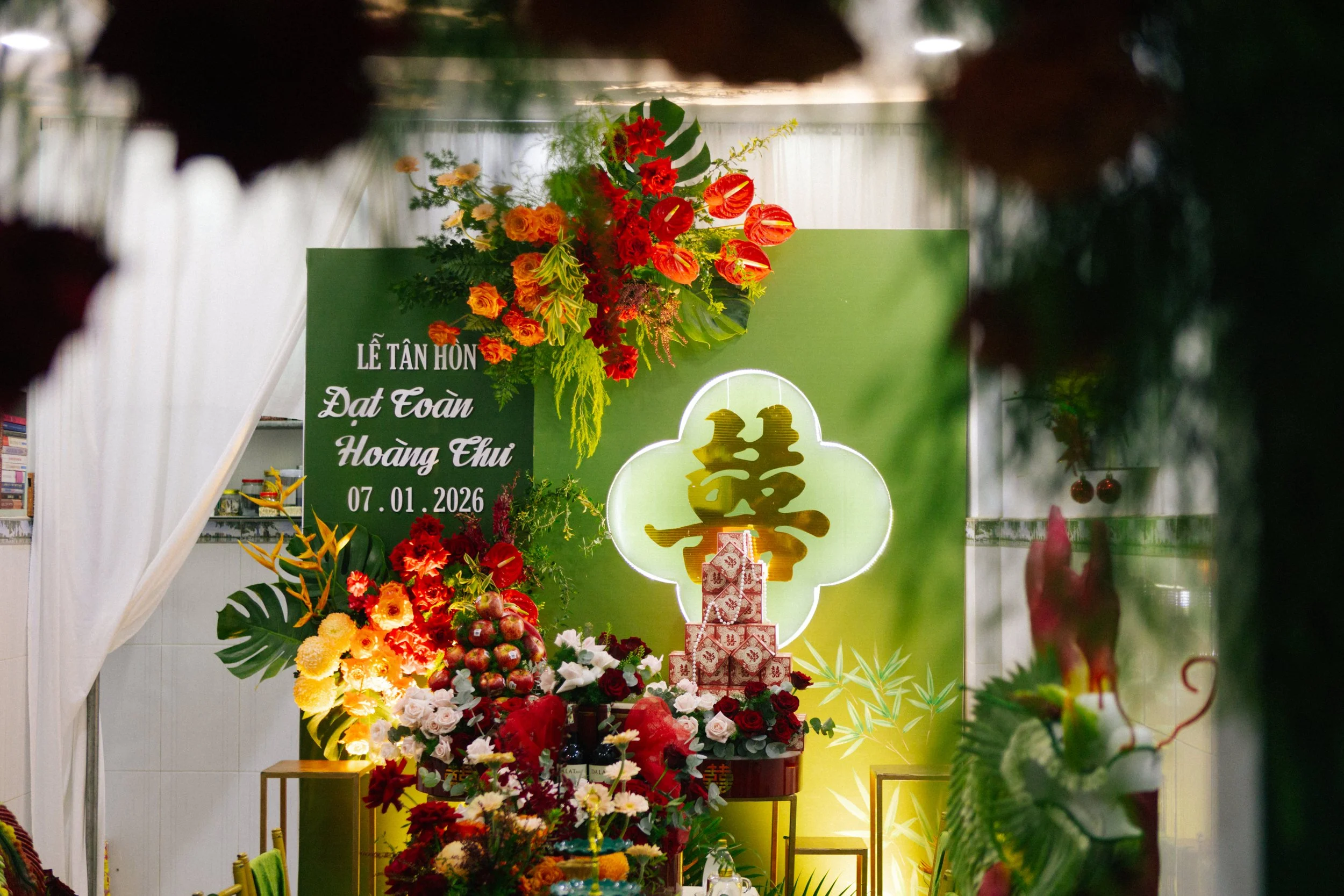 Flower arrangement and decorations for a wedding celebration, with a green backdrop, a large Chinese character for double happiness, and a sign indicating the wedding date as January 7, 2026.