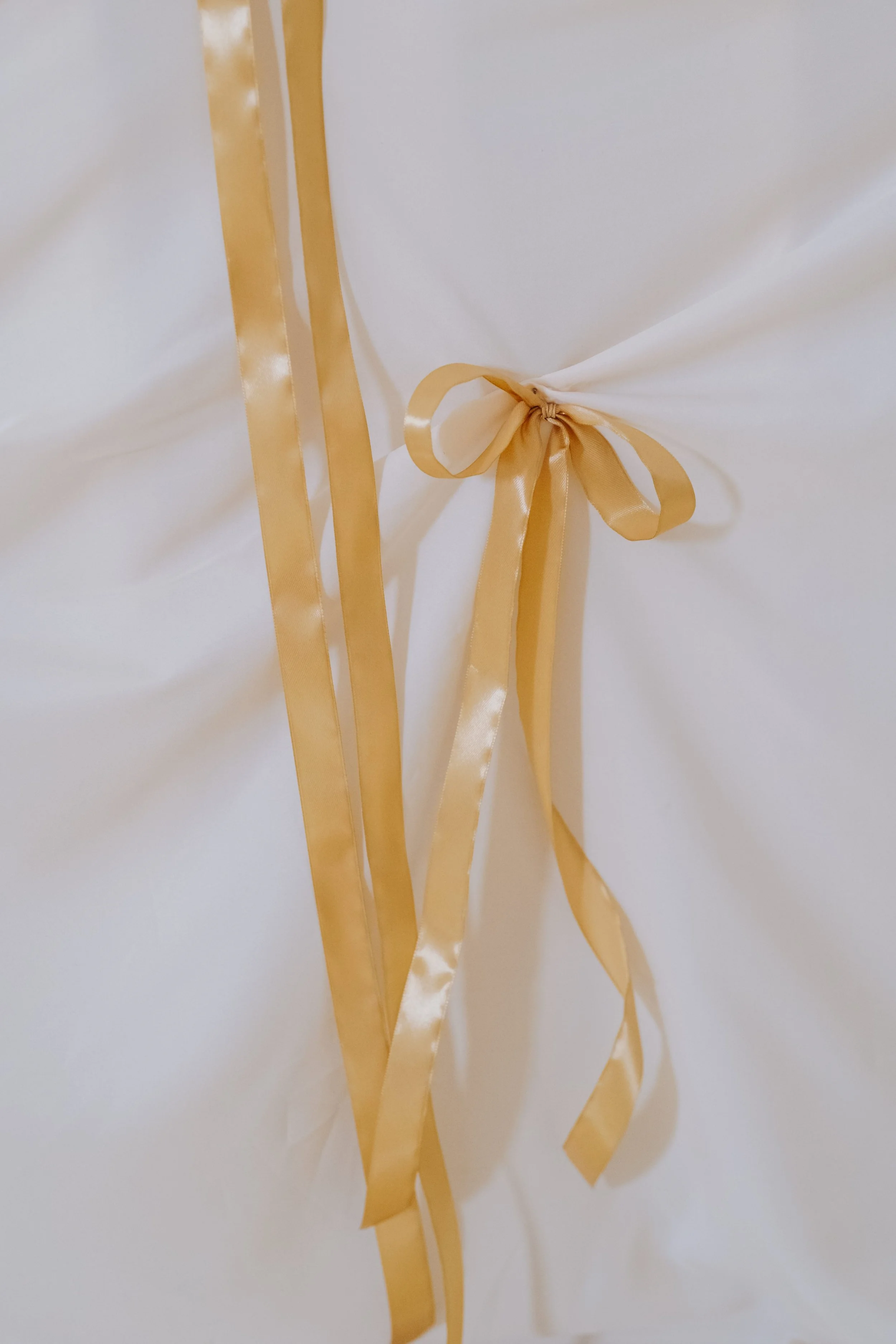 Cream-colored fabric with a gold satin ribbon tied in a bow.
