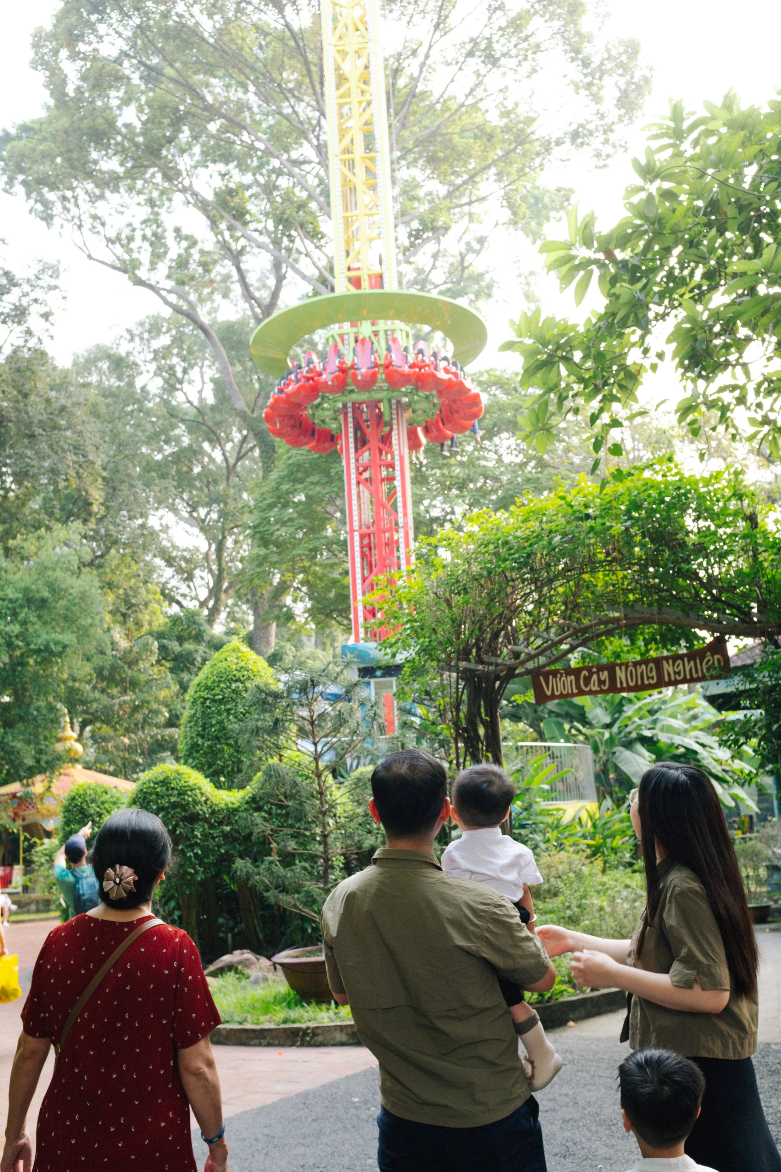 People looking at a tall amusement park ride with a red and yellow color scheme and a circular gondola full of riders.
