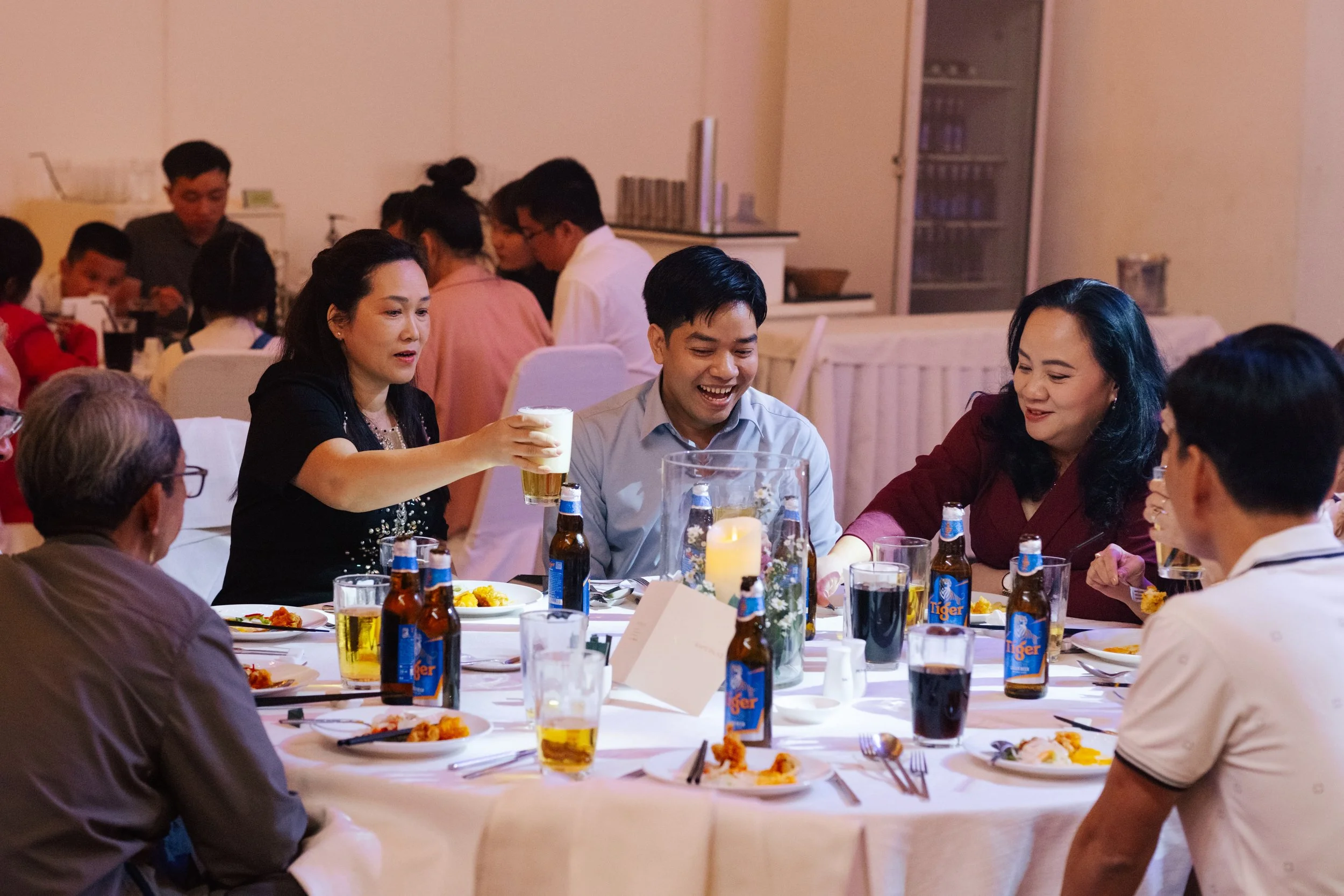 People gathered around a table at a social event, sharing drinks and food, with some people smiling and talking.
