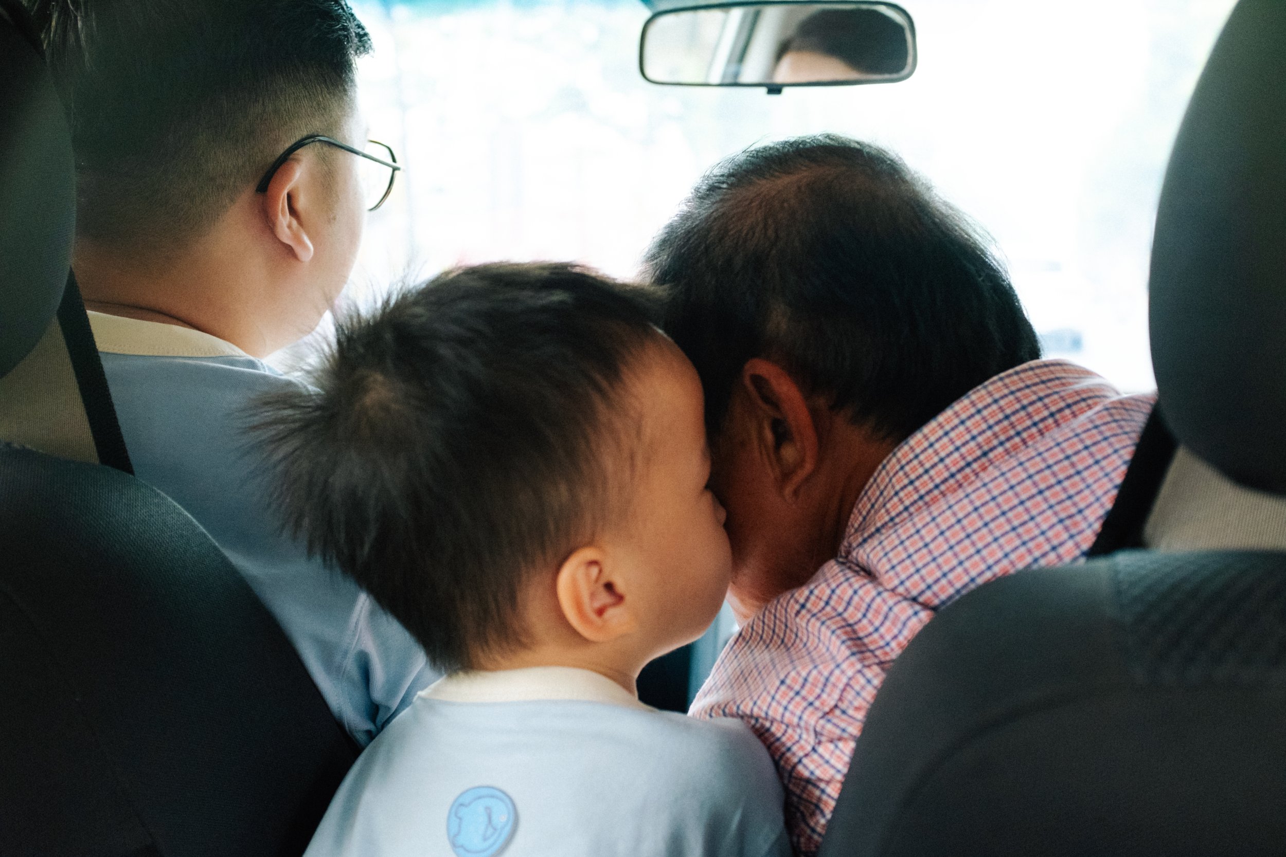 Three people, two children and an older man, sitting in a car, leaning close to each other with their heads touching, sharing a moment of affection.