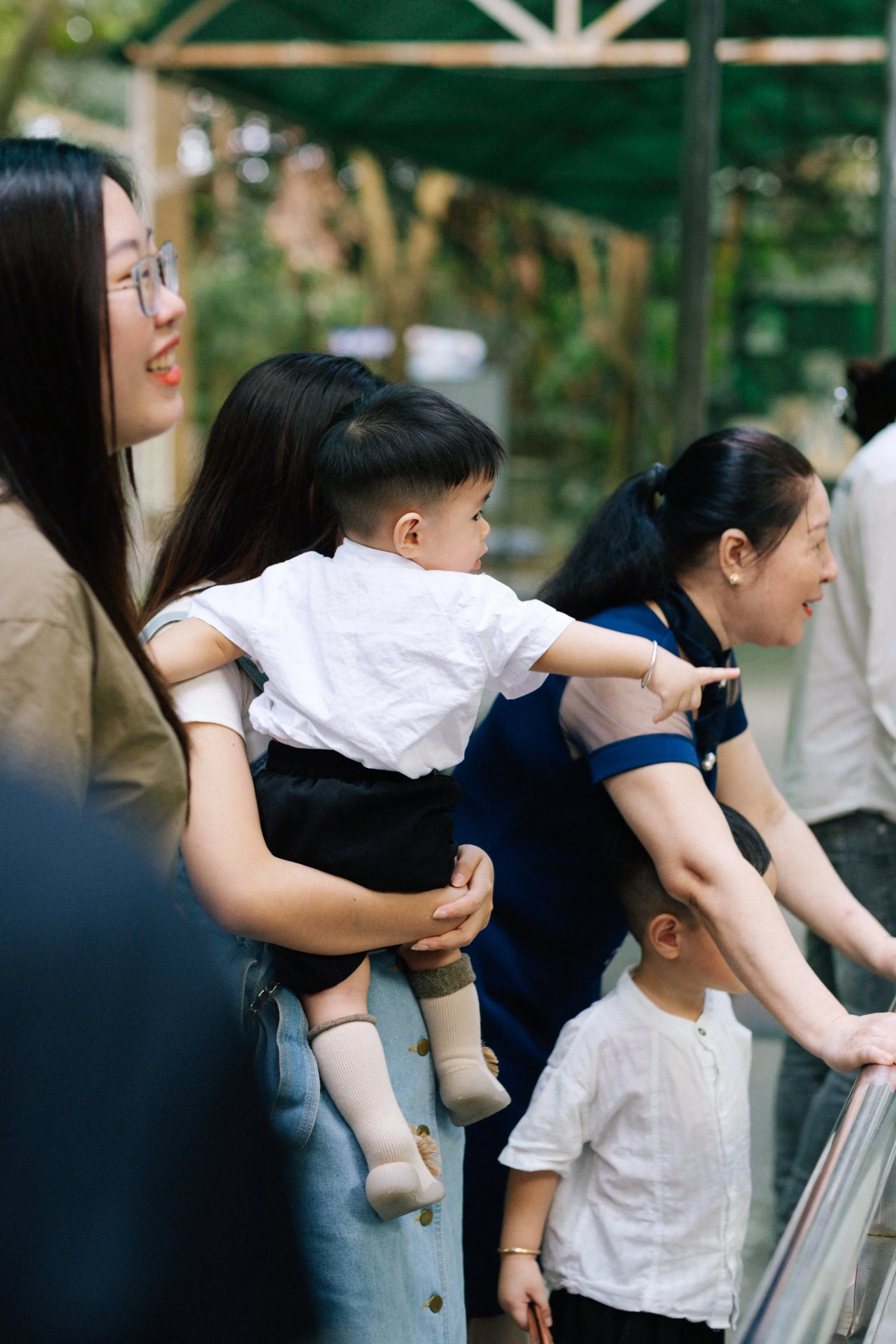 A group of people, including women and children, looking at something to the right outdoors during daytime.