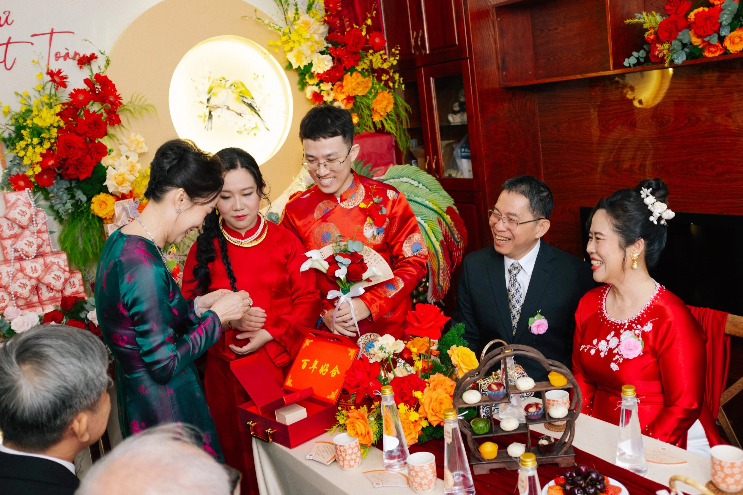 A traditional Vietnamese wedding celebration with the bride and groom dressed in red, surrounded by family members and colorful floral decorations.