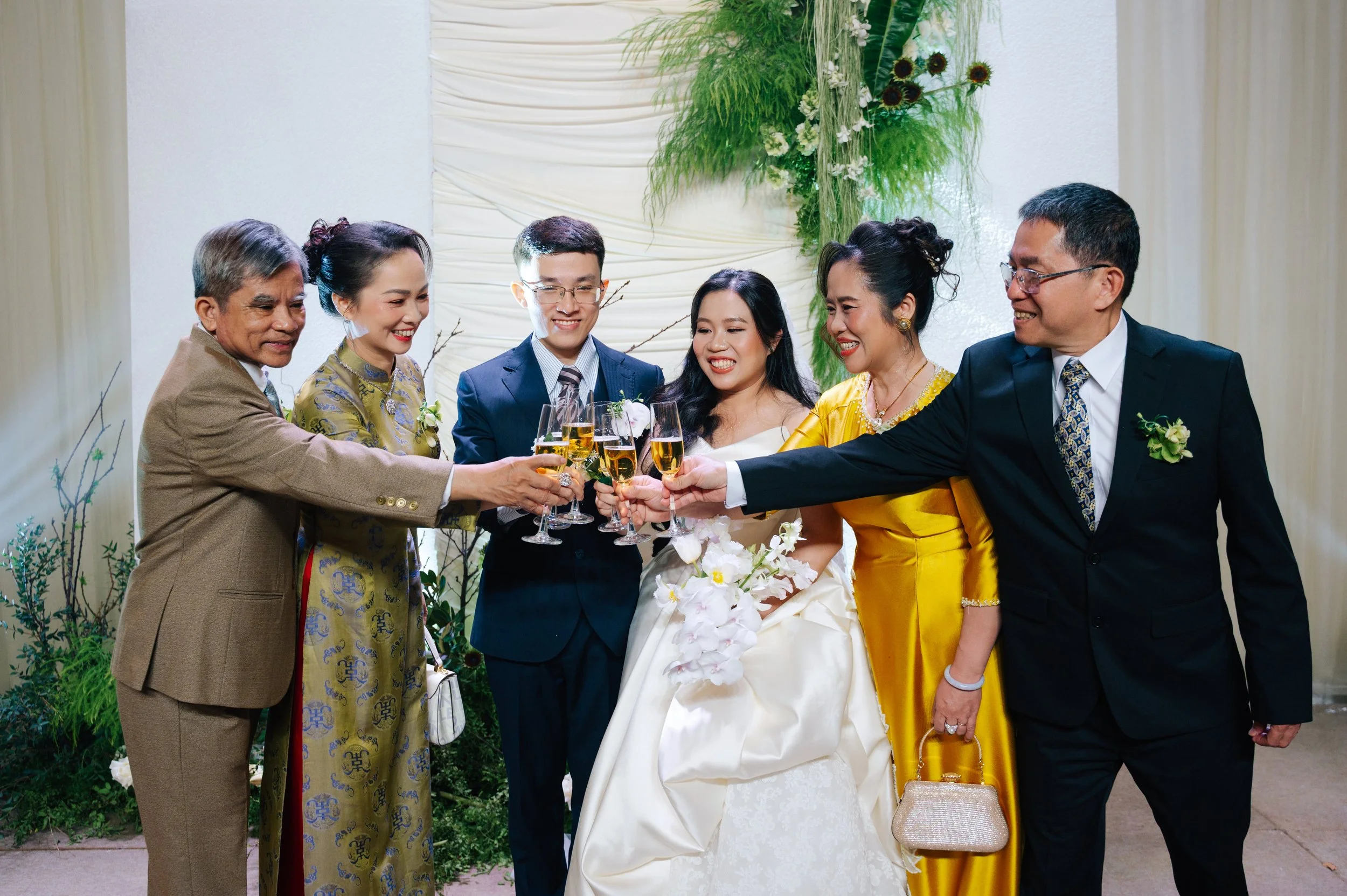Group of seven people, including a bride and groom, raising glasses of champagne in celebration at a wedding reception.