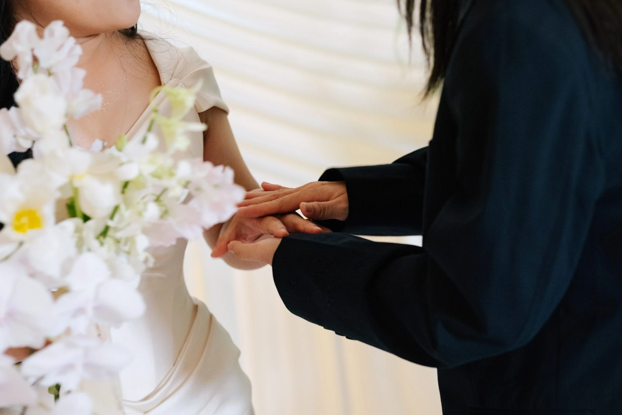 A person in a black suit holding the hands of a woman in a white dress during a wedding ceremony.