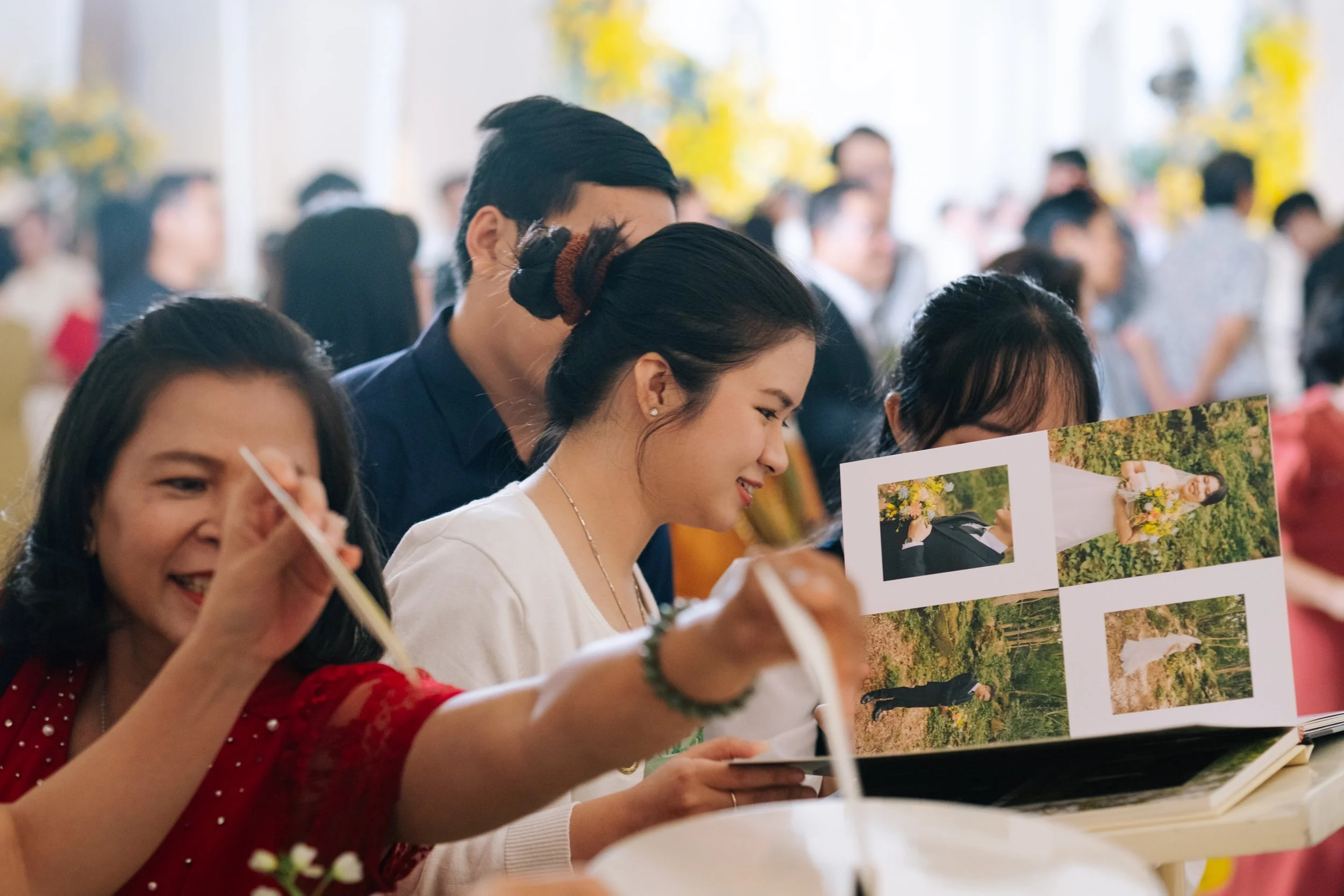 People at a gathering looking at photo albums with outdoor photographs, smiling and engaging with each other.