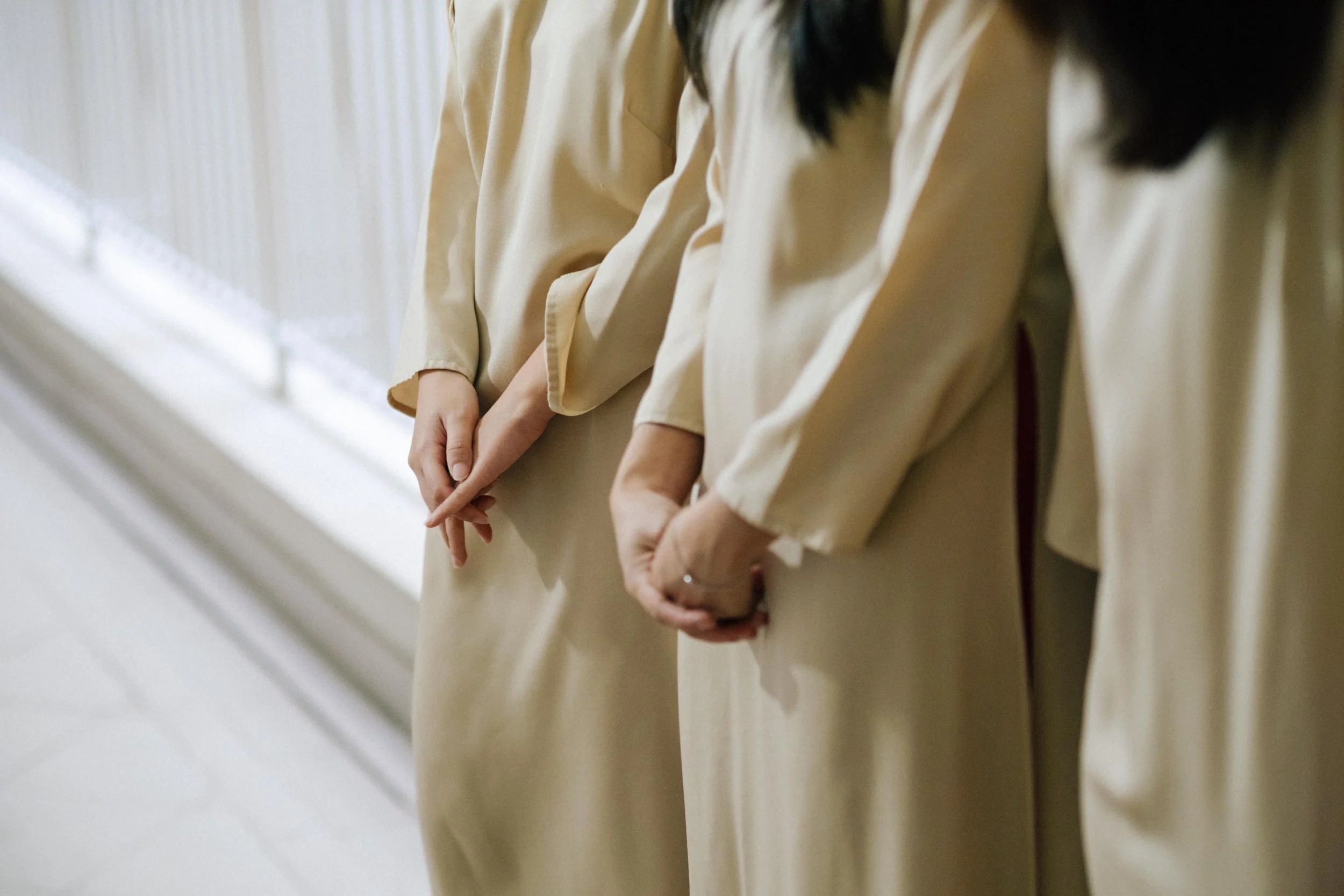 Three women wearing beige dresses standing side by side with their hands clasped in front of them.