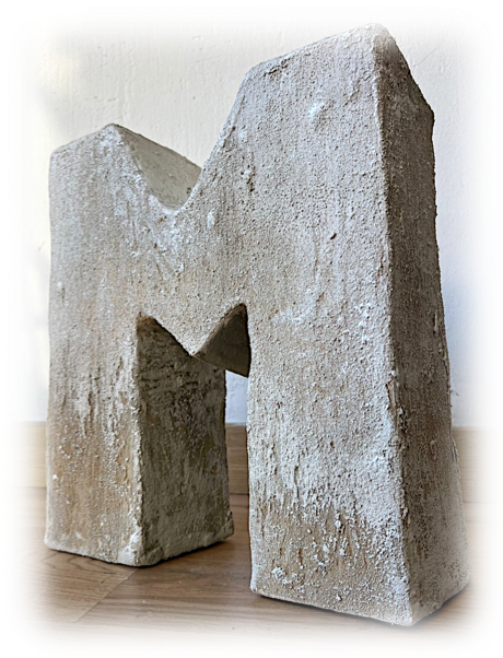 Letras de piedra de color gris en forma de 'M' sobre superficie de madera.