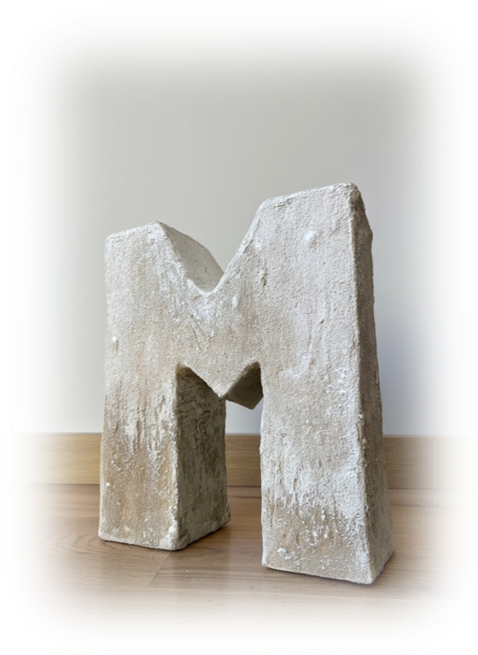 Letra mayúscula 'M' de piedra en piso de madera