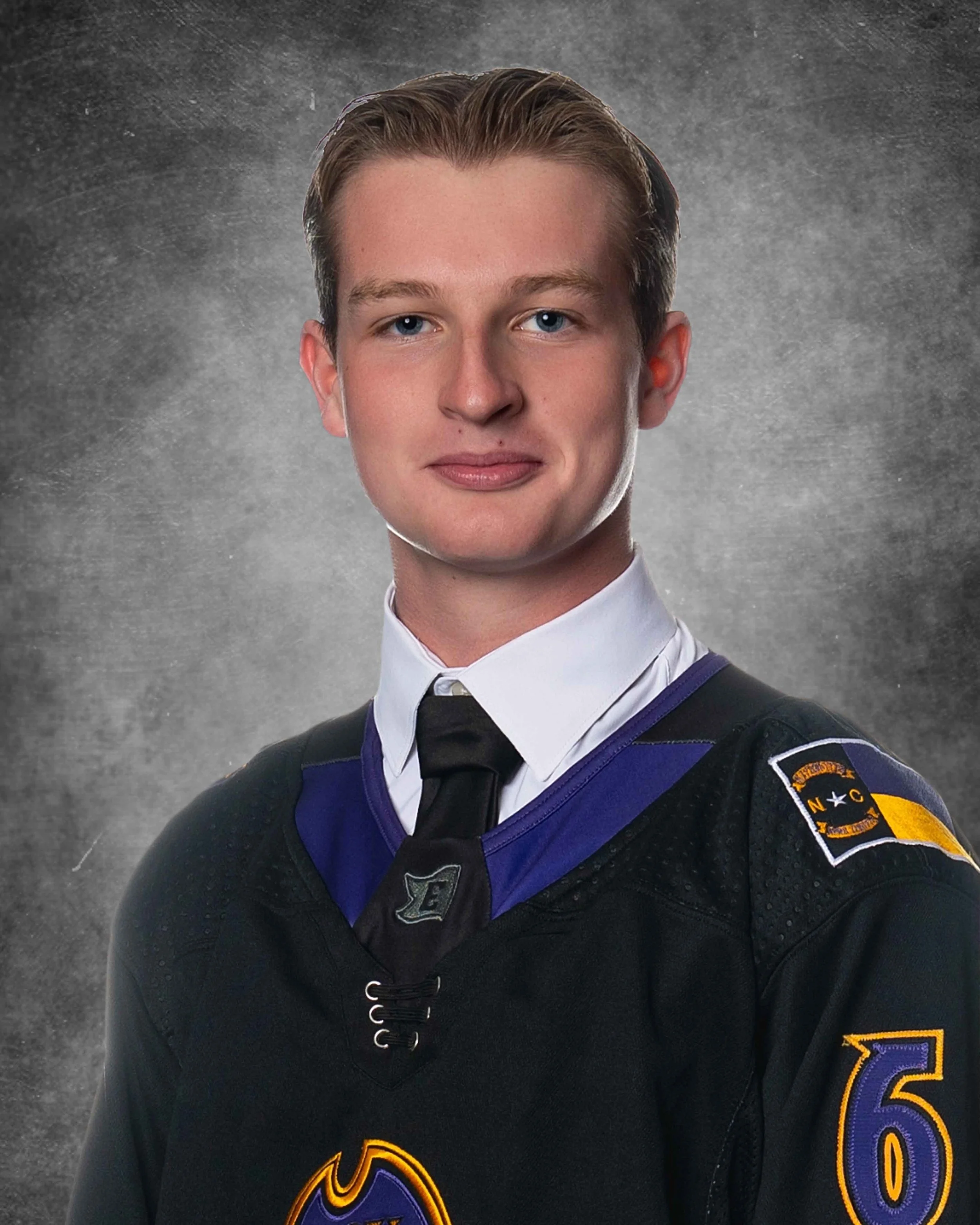 Young man in a graduation gown and cap, smiling against a dark grey background.