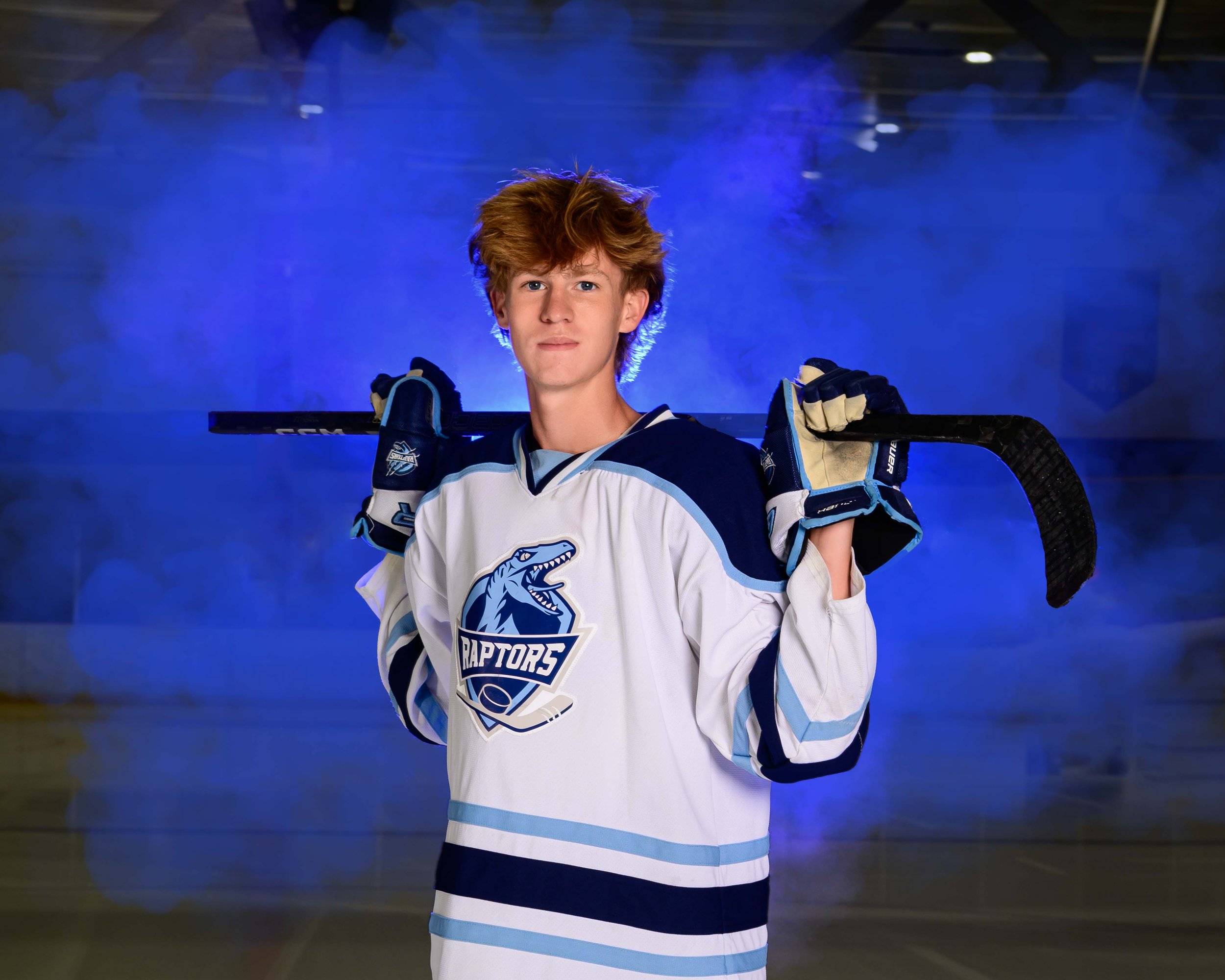 Young hockey player in a Toronto Raptors jersey holding a hockey stick on an ice rink with blue lighting and smoke.