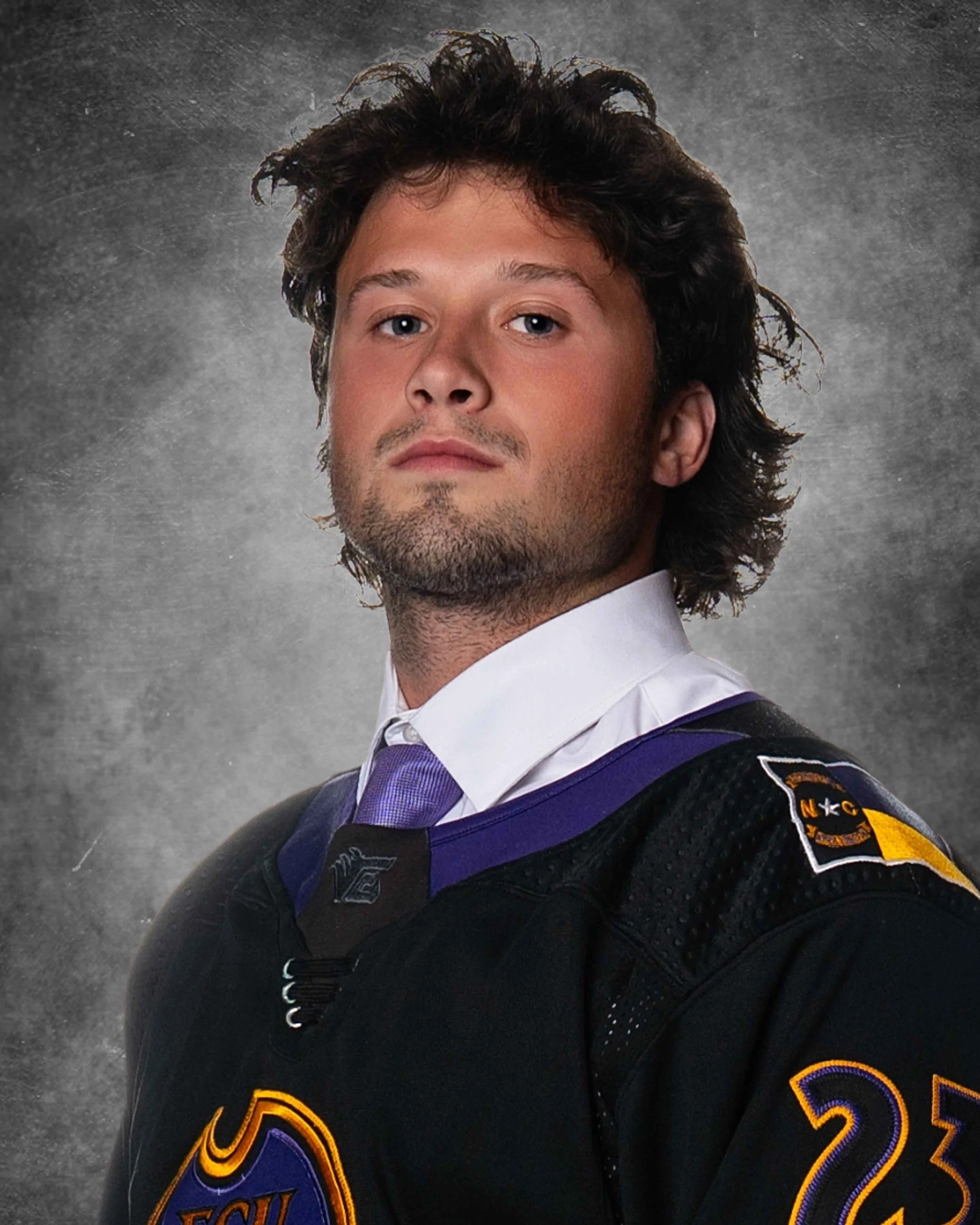 Close-up of a man with curly dark hair and a short beard wearing a hockey jersey with a patch on the sleeve, Hockey headshot