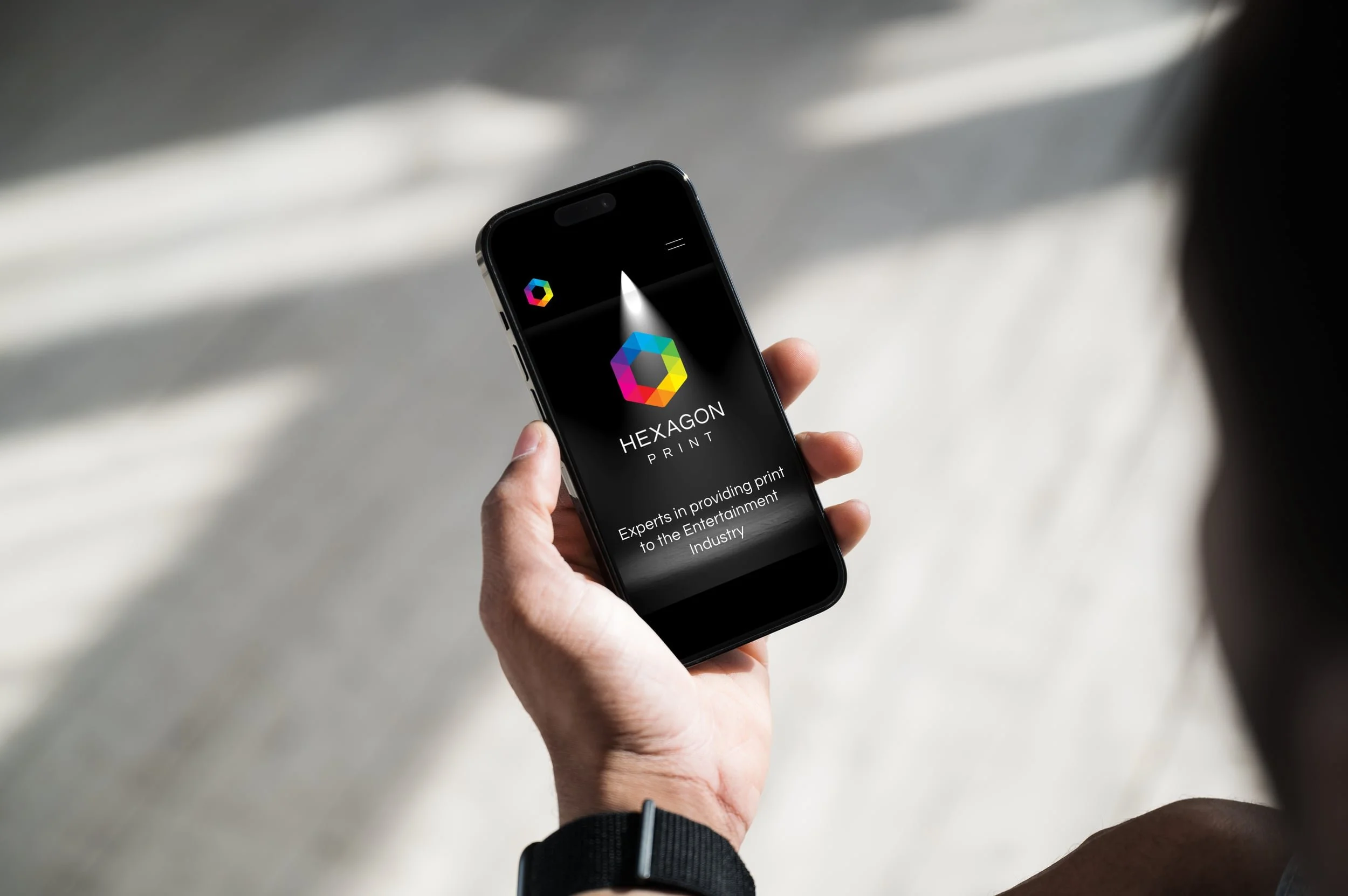 A person holding a smartphone displaying the Hexagon Print logo with a colorful hexagon icon and the text 'HEXAGON PRINT' on a black background.