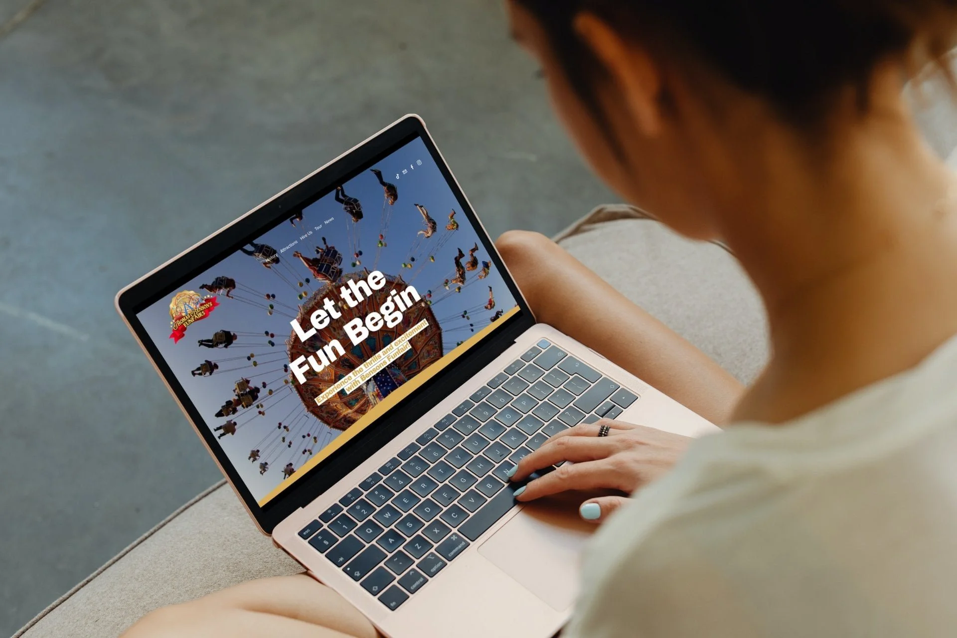 A person sitting on a concrete surface looking at a tablet with a carnival ride and the text 'Let the Fun Begin'.