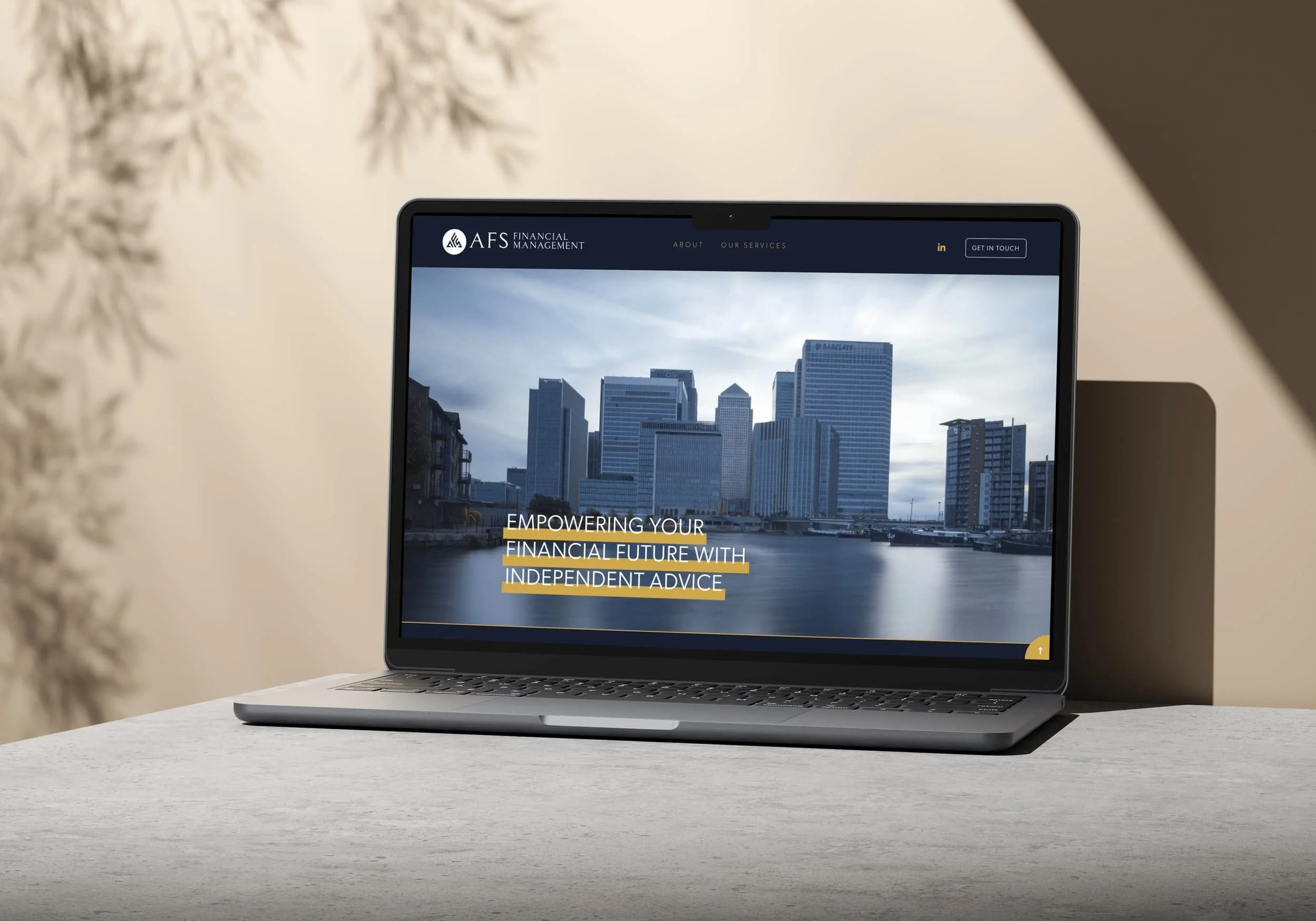 Laptop displaying a city skyline with modern buildings and the text "Empowering your financial future with independent advice" on a white desk, with a blurred background of a beige wall and some decorative white tree branches.