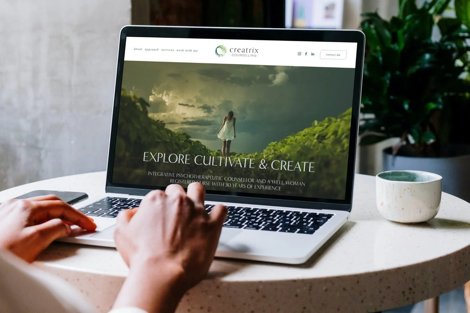 Person working on a laptop displaying a website for a counseling service called Creatrix Counseling, featuring a woman in a white dress standing in a lush green landscape under a cloudy sky.