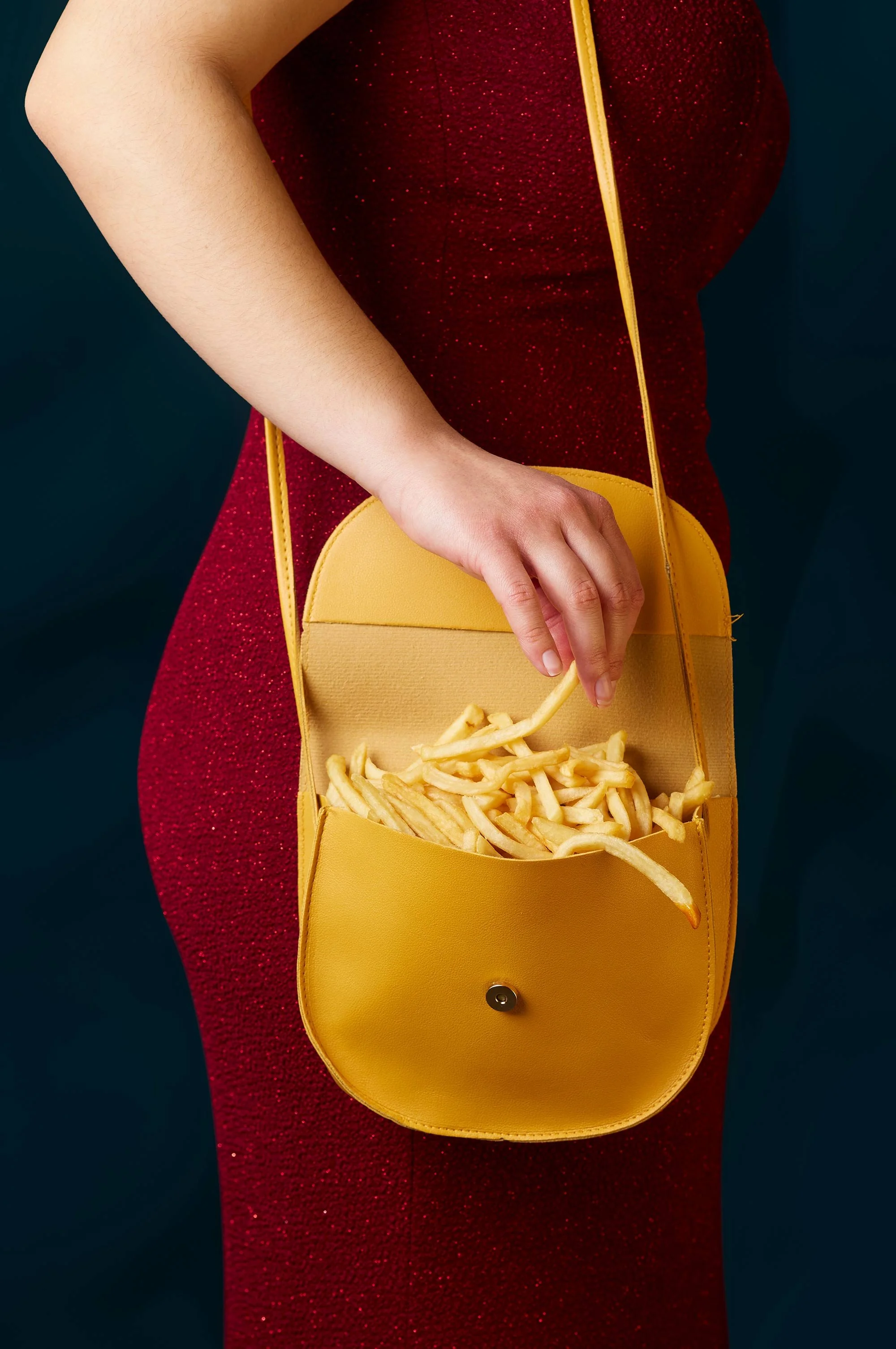 Yellow purse filled with fast food French fries hanging on arm of woman in sparkly red dress.